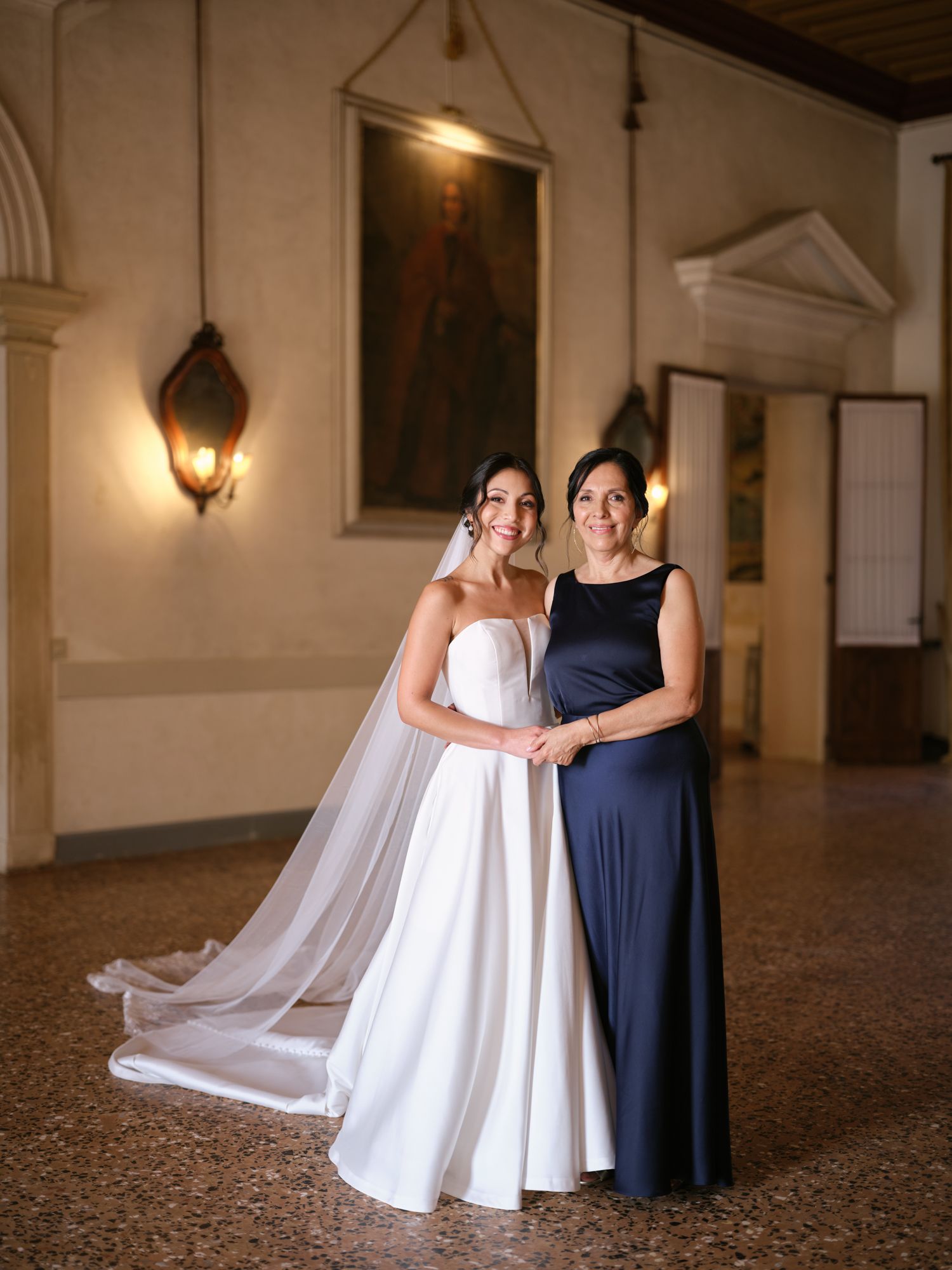 A flowing white dress and navy gown create elegant silhouettes against a classical interior with stone floors.