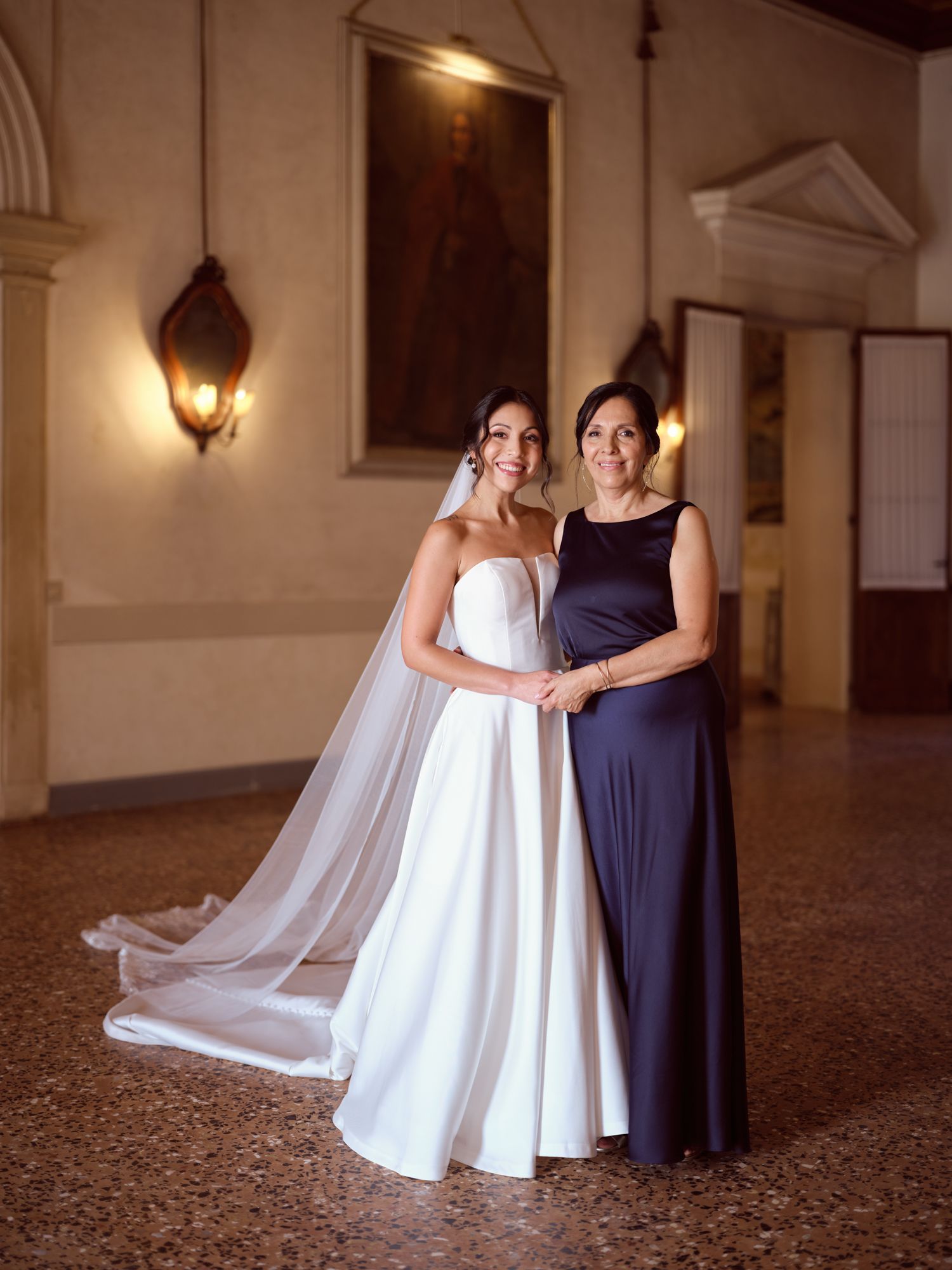 A wedding dress and navy blue bridesmaid gown displayed together in an elegant hallway with warm lighting.