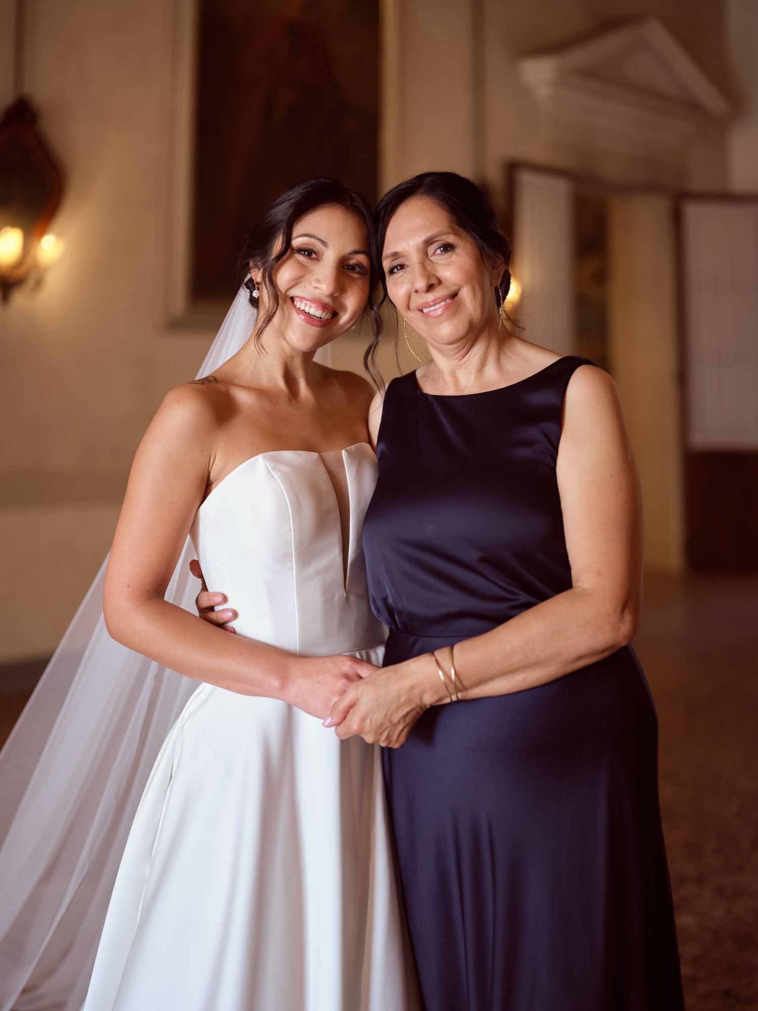 A bride in white and someone in navy blue share a joyful embrace while posing for photos at a wedding.
