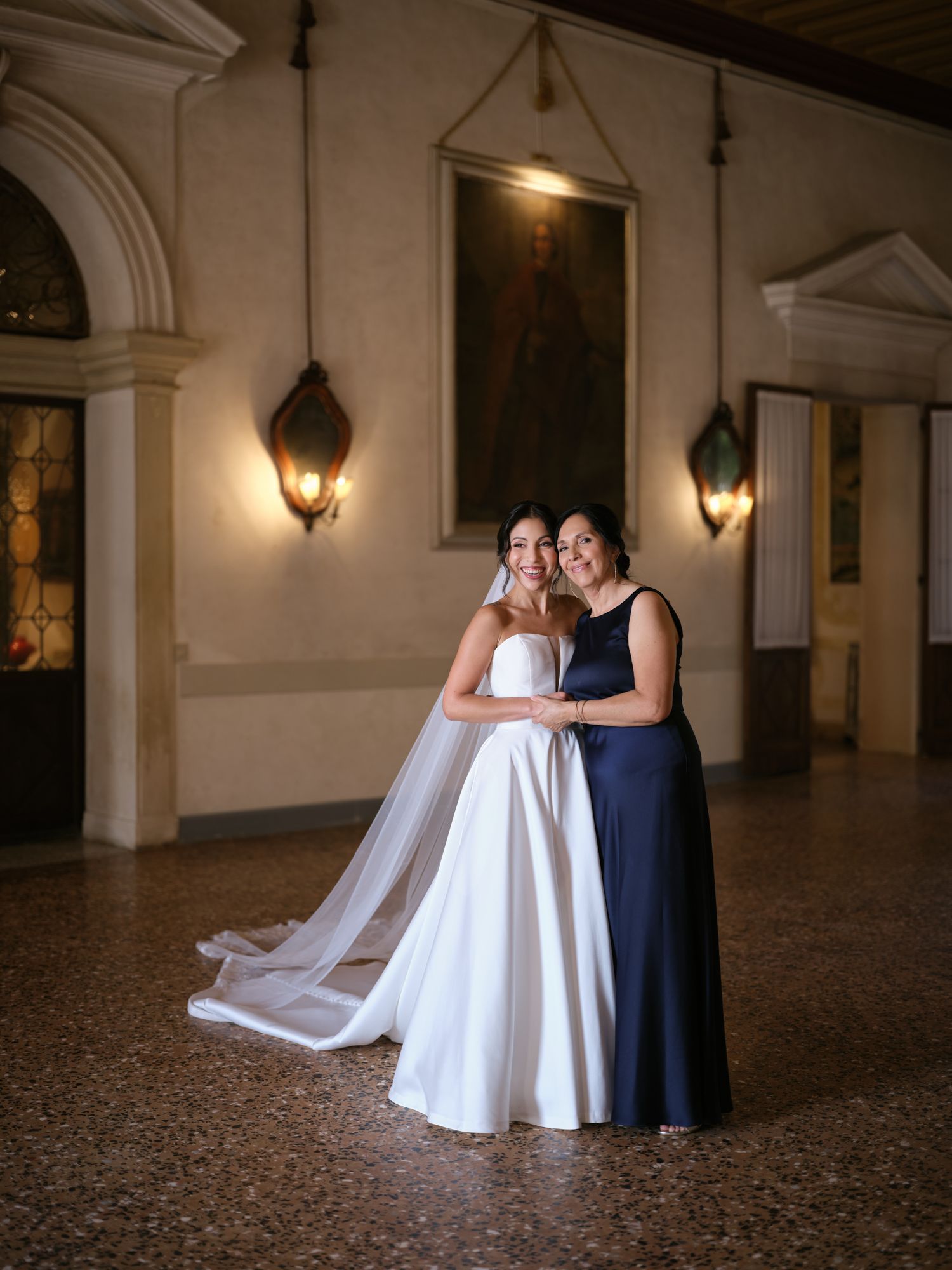 A couple in wedding attire shares an intimate moment in an elegant hallway with arched columns and warm lighting.