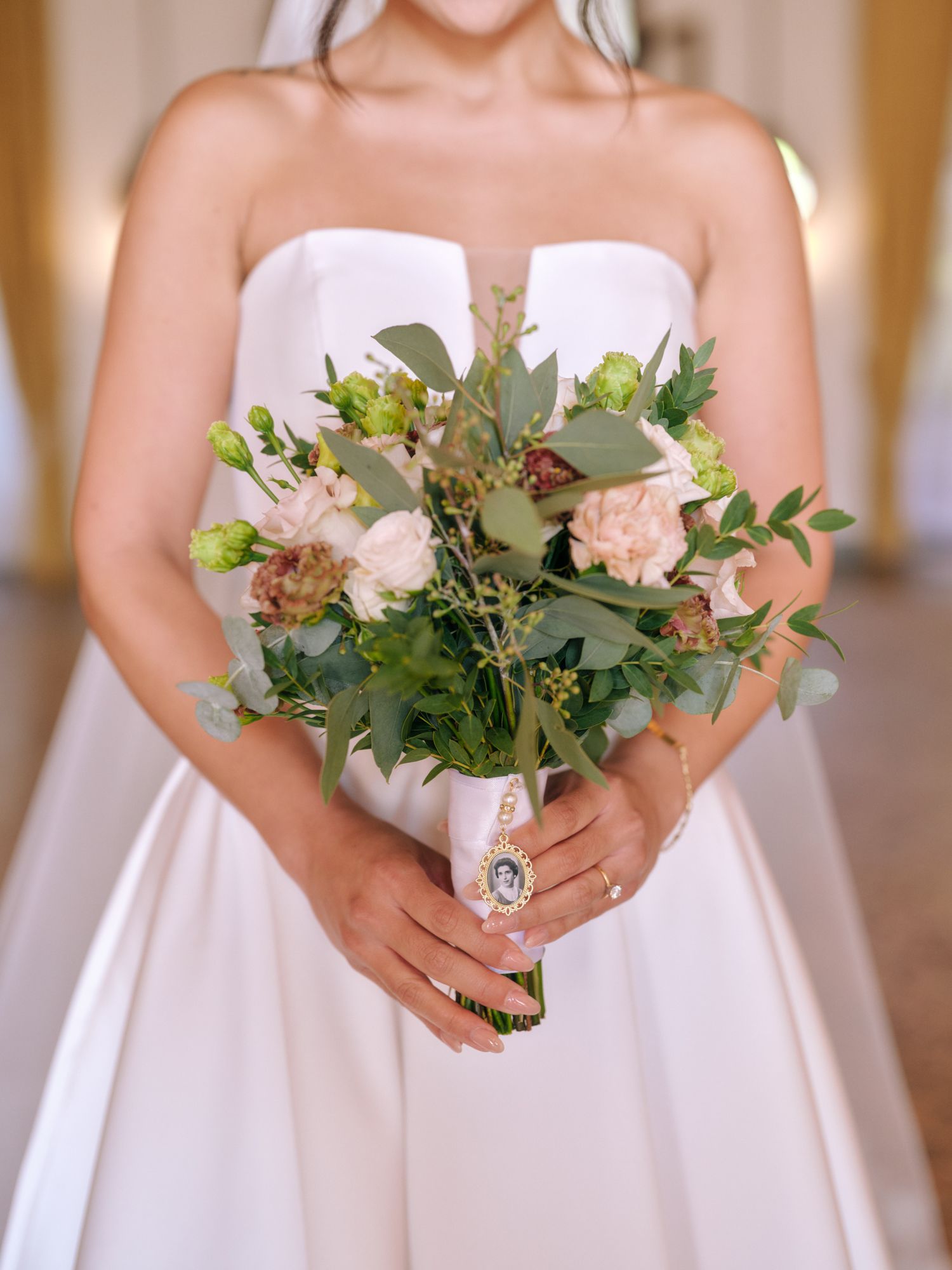 Bridesmaids in white strapless dresses hold elegant greenery bouquets at a formal wedding ceremony.