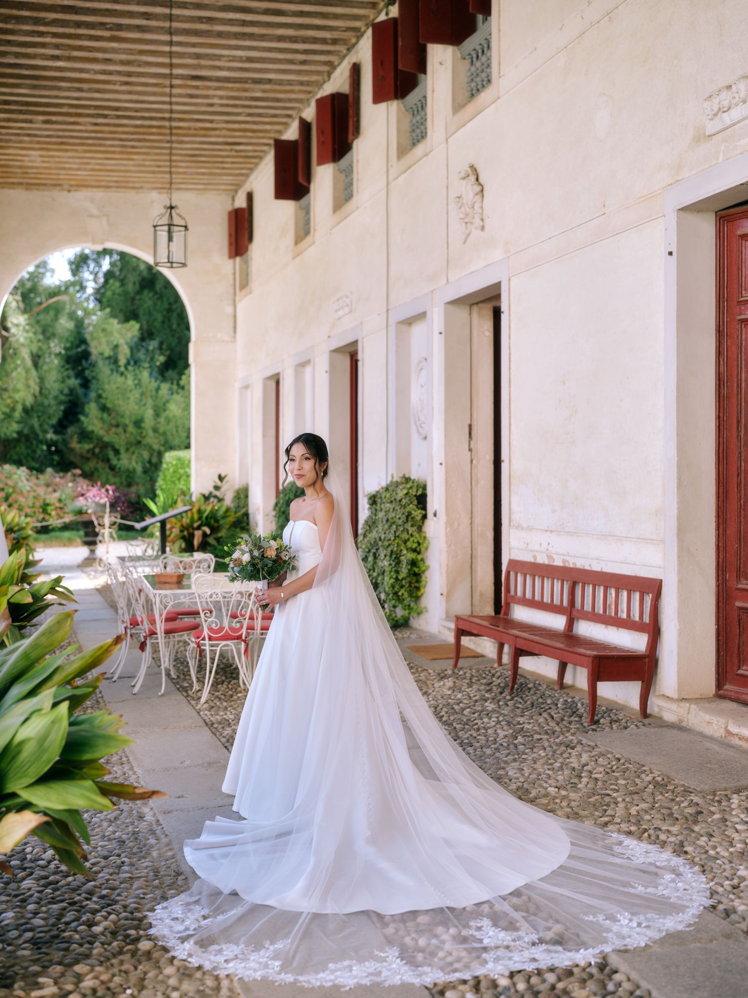 A series of elegant bridal portraits showing a flowing white wedding dress with a long train along a rustic covered walkway.