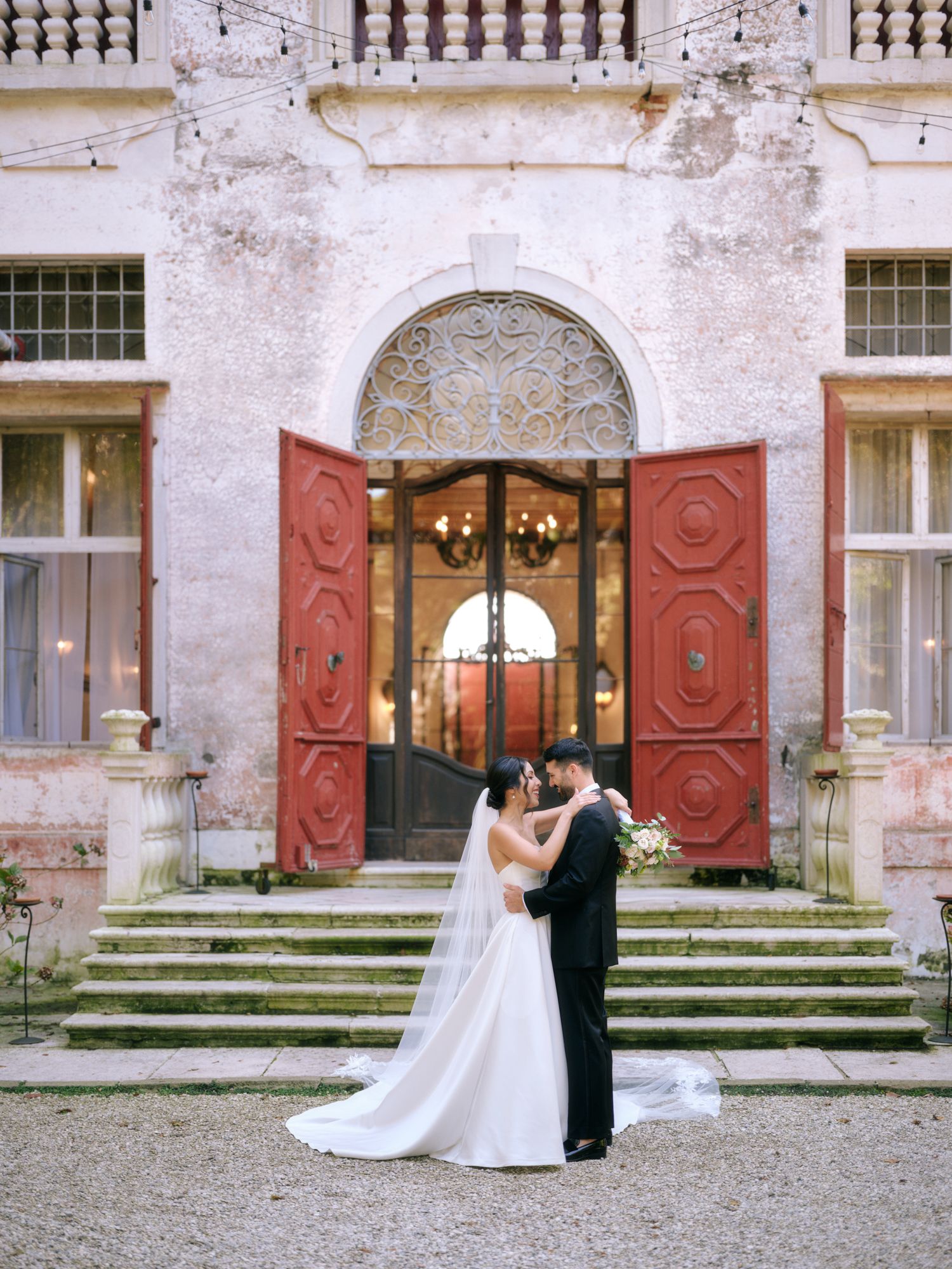 A romantic wedding couple shares a dance sequence in front of a historic building with red doors and stone steps.