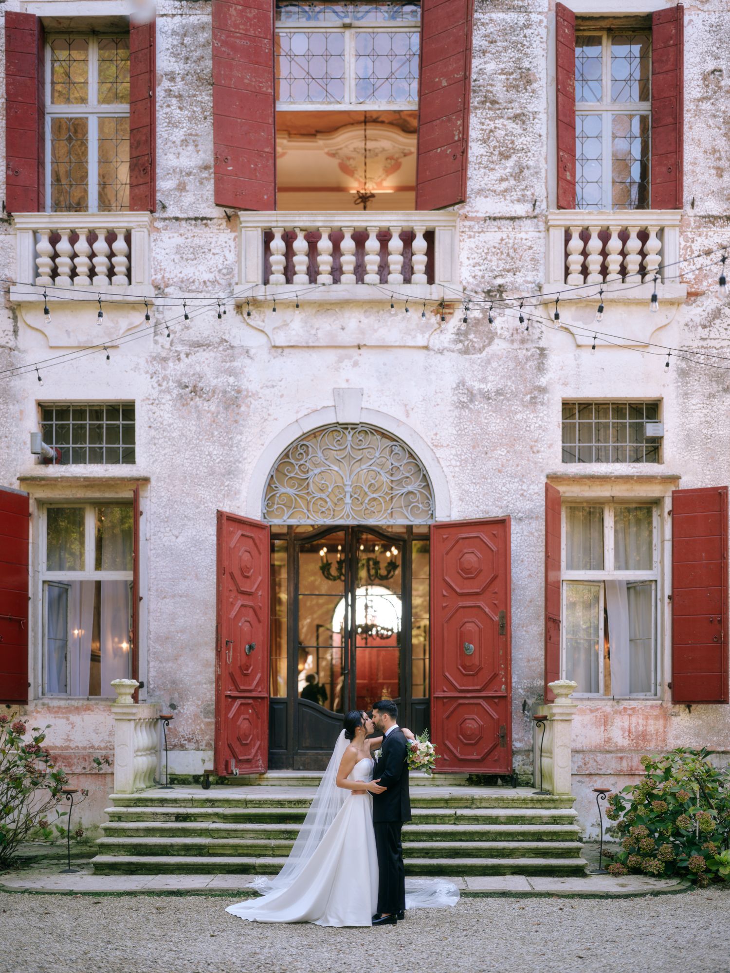 A sequence of wedding photos showing a couple walking through an elegant red brick mansion with ornate doors and steps.
