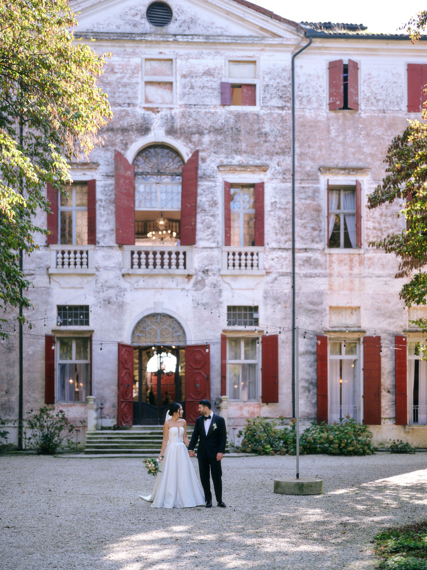Historic stone villa with elegant columns and red shutters features a romantic courtyard setting for an intimate wedding.