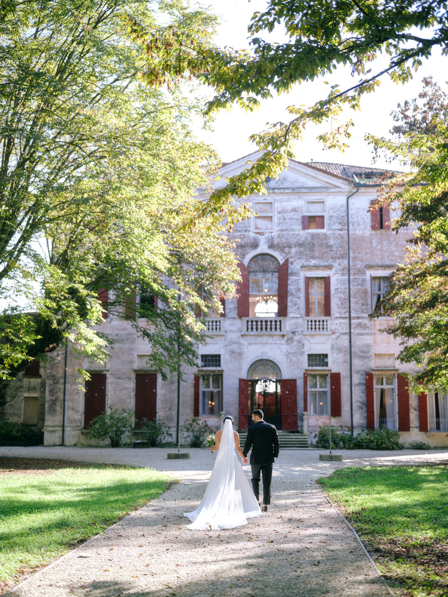 Historic stone mansion with arched windows and doorways surrounded by lush green trees creates an elegant backdrop.