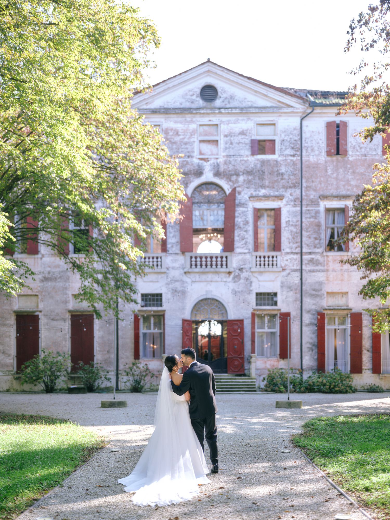 Historic stone mansion with white facade and arched windows serves as elegant backdrop for romantic wedding photography.