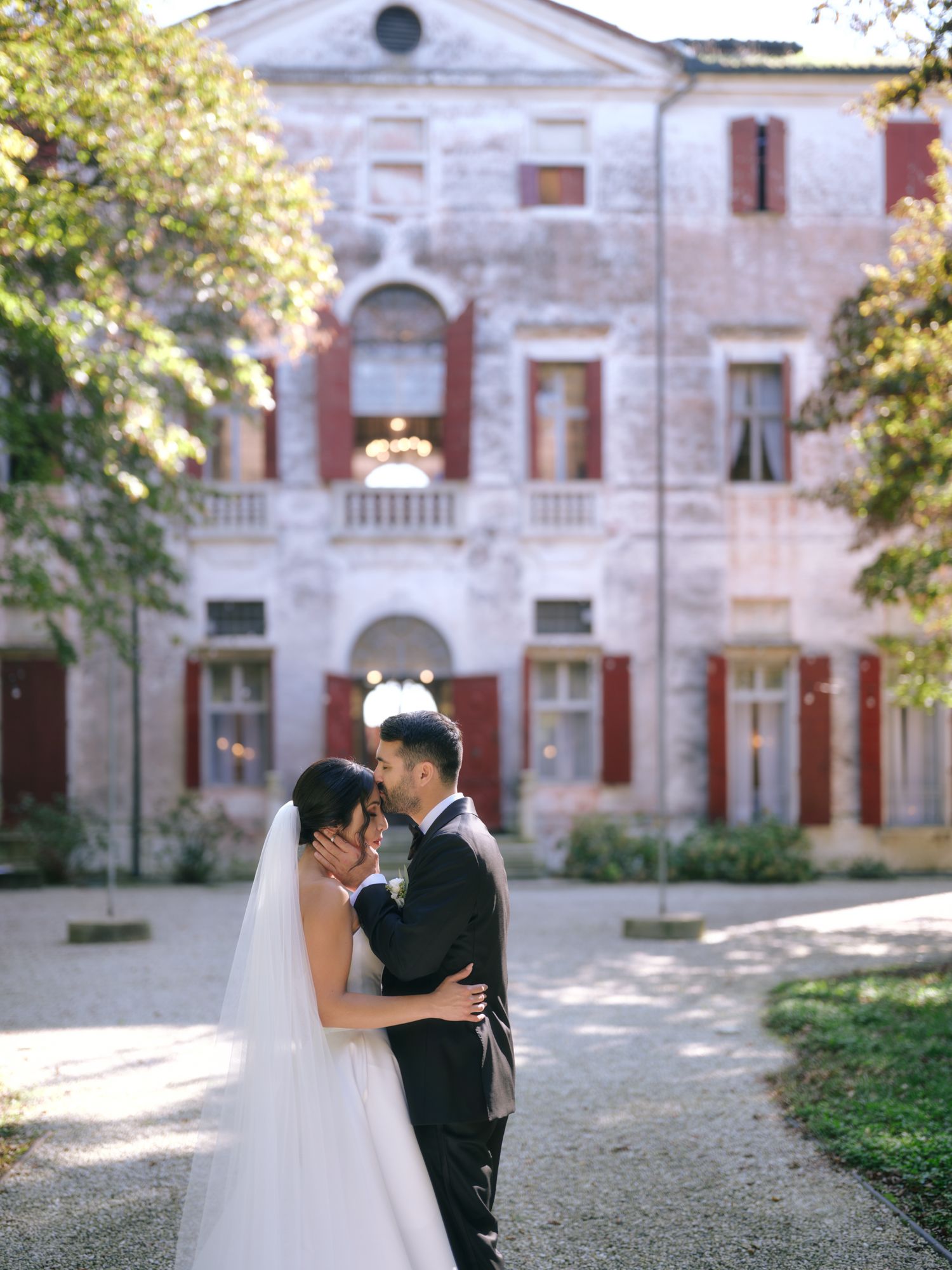 Newlyweds share intimate moments in a courtyard of a grand historic building with brick and stone facade.