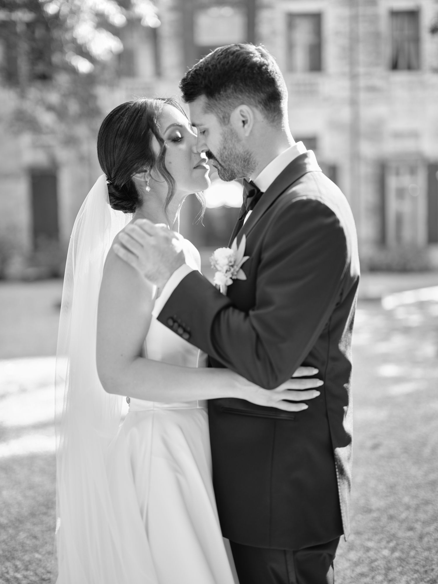 A romantic black and white wedding portrait of a couple embracing outdoors with a beautiful architectural backdrop.