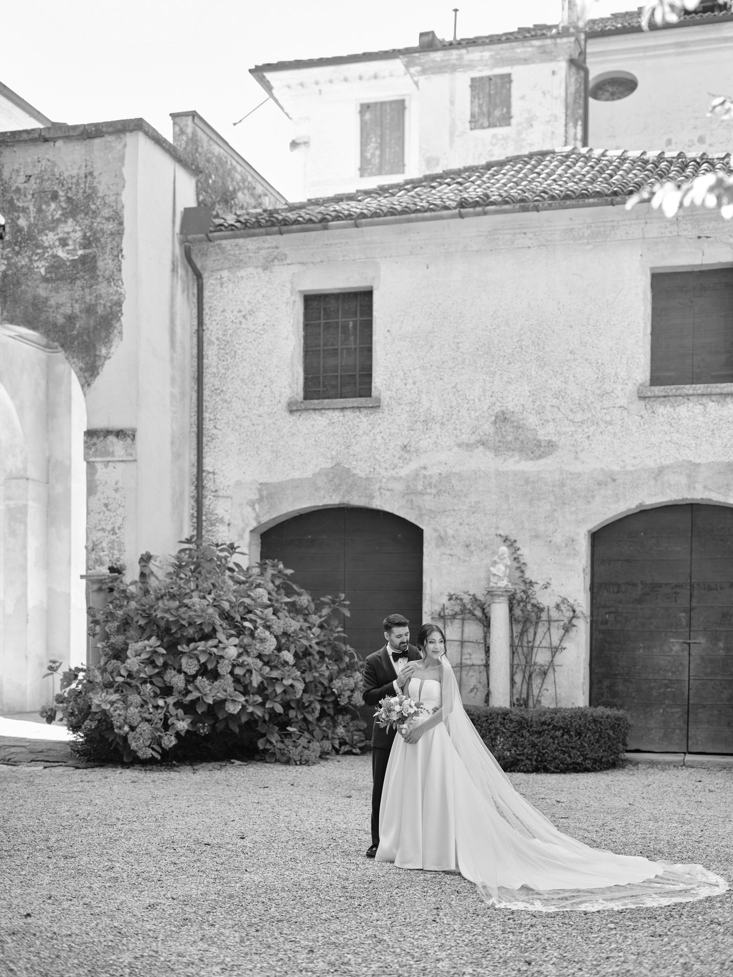 A sequence of black and white wedding photos showing a bride in a flowing gown against rustic stone buildings and archways.