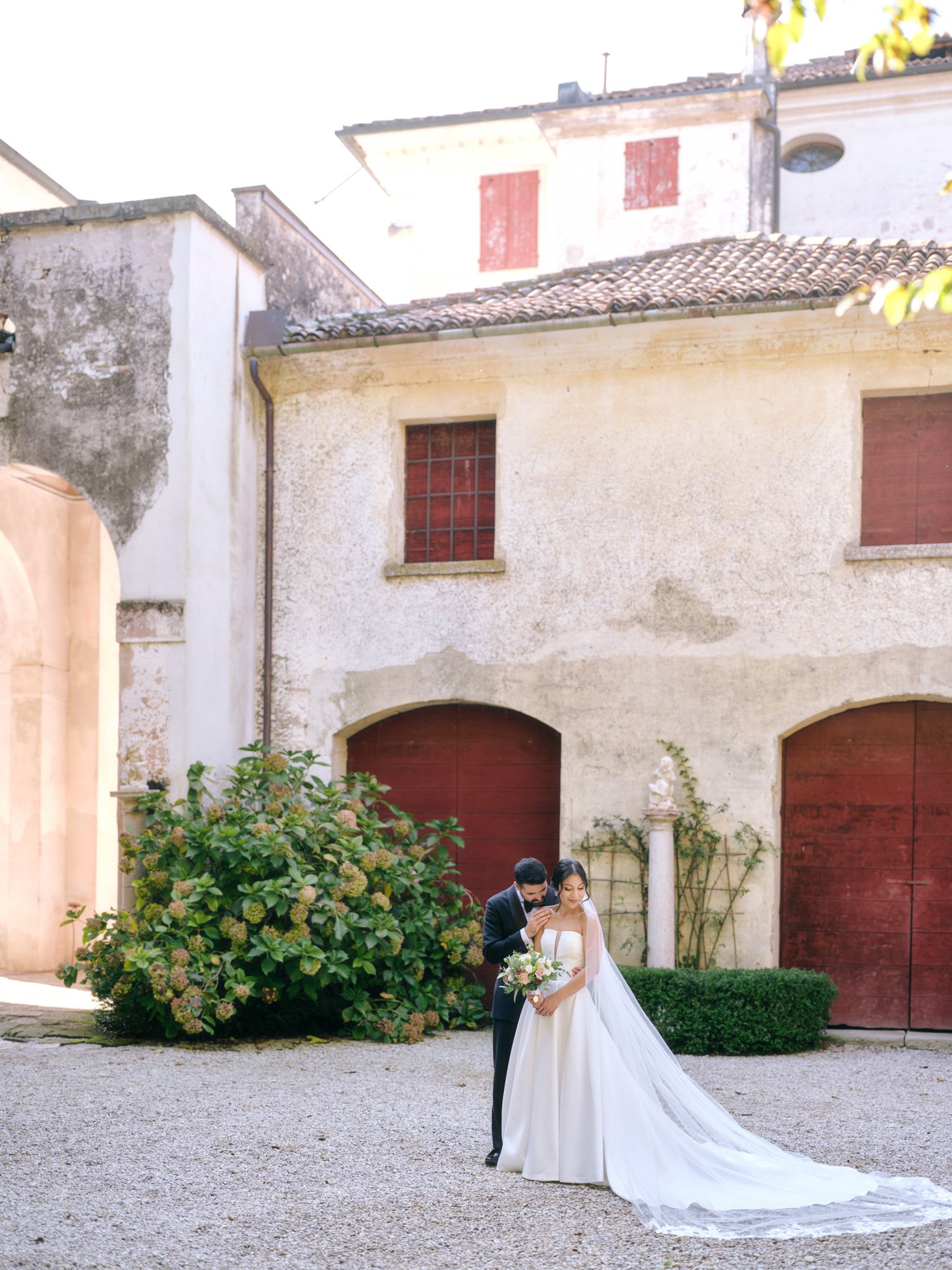 A wedding couple shares an intimate moment in front of a Mediterranean villa with rustic red doors.