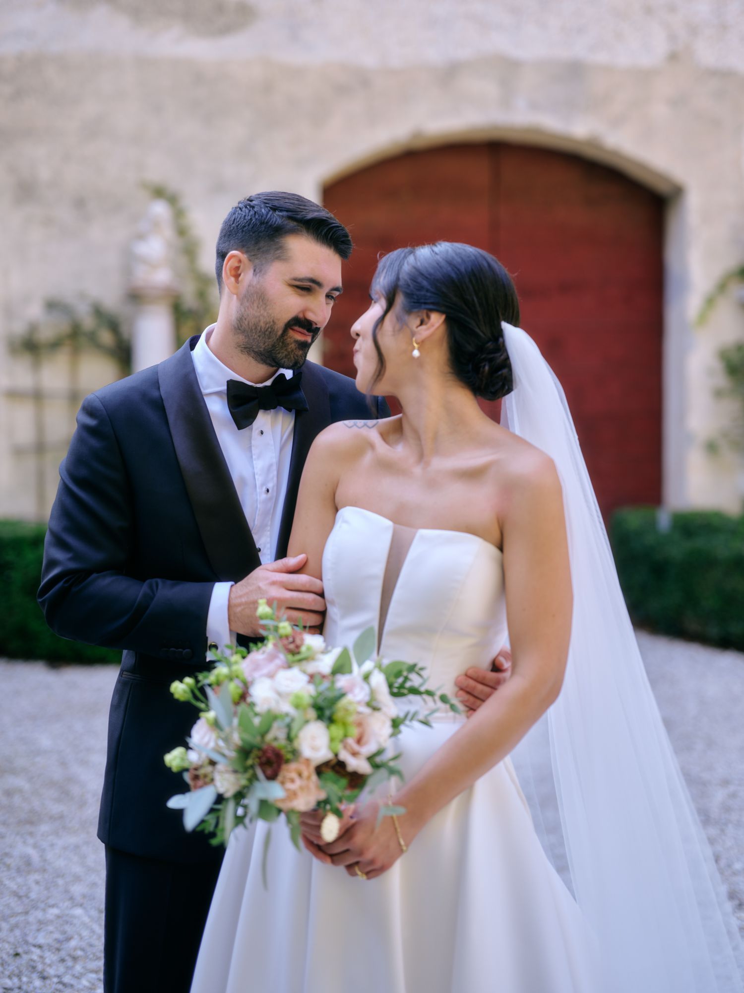 A romantic wedding couple embraces in a series of candid moments against a stone wall backdrop with elegant floral bouquet.