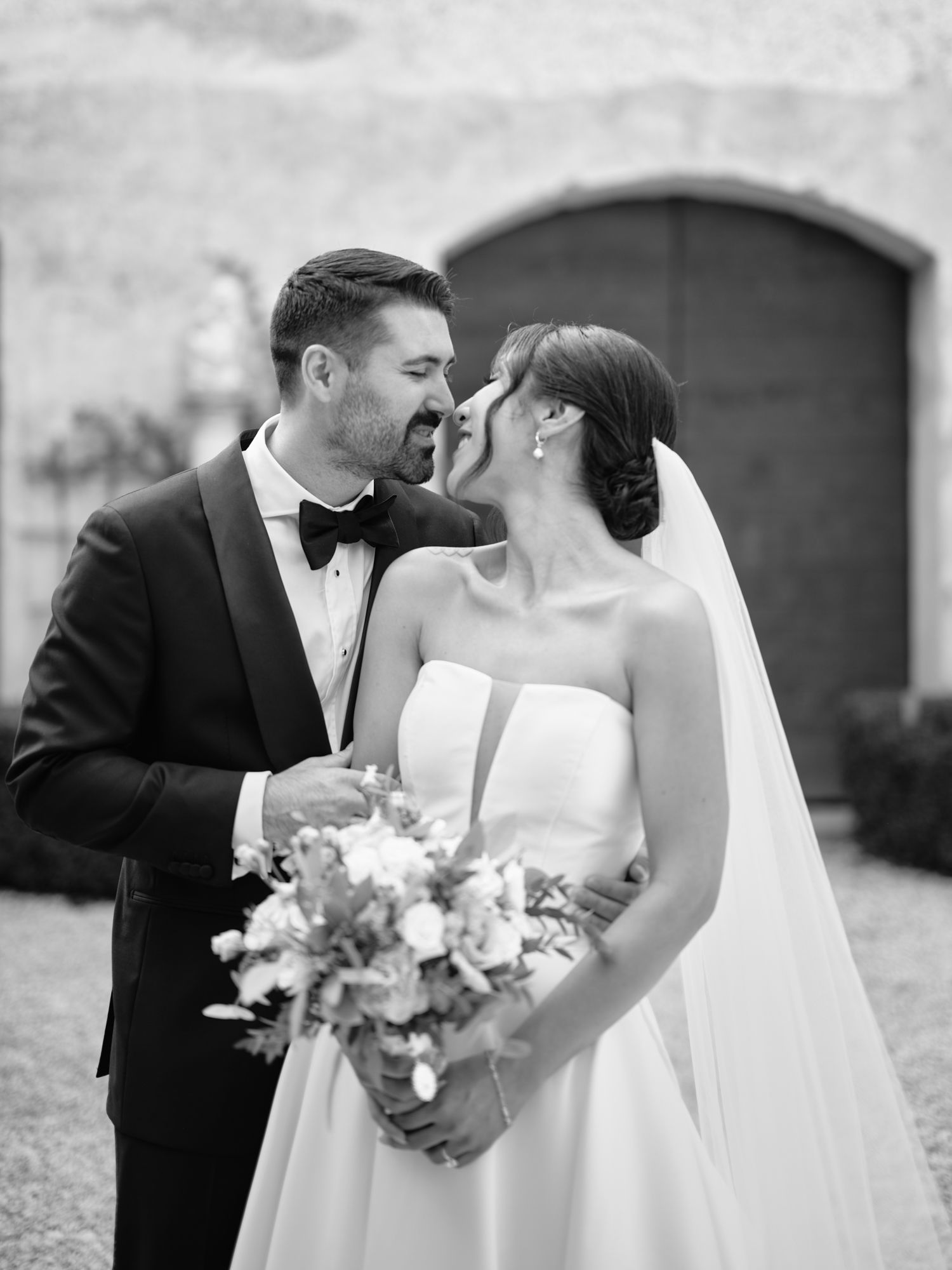 A romantic black and white wedding photo showing a couple sharing an intimate moment with the bride holding a floral bouquet.