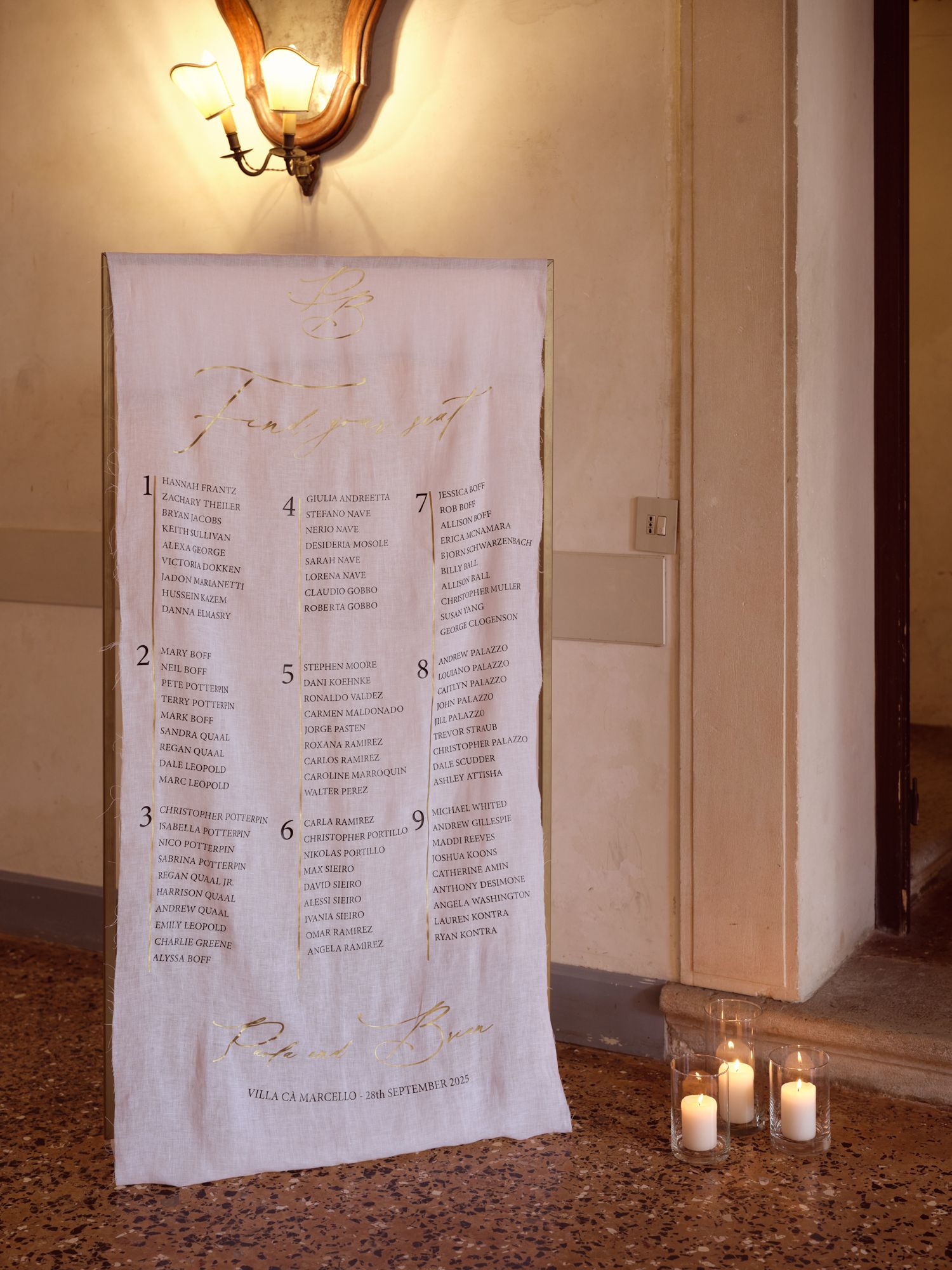 Four fabric panels with text hang on a beige wall illuminated by warm sconces in an elegant hallway setting.