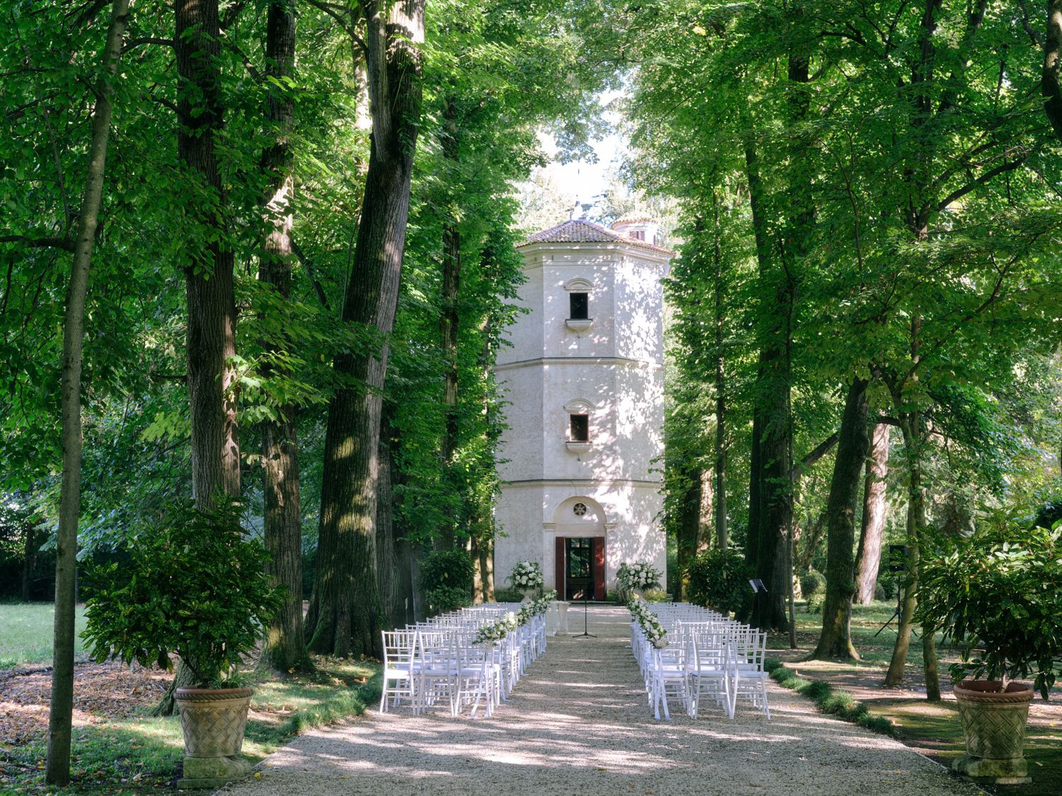 A tree-lined path leads to a white church building in a lush green park setting.