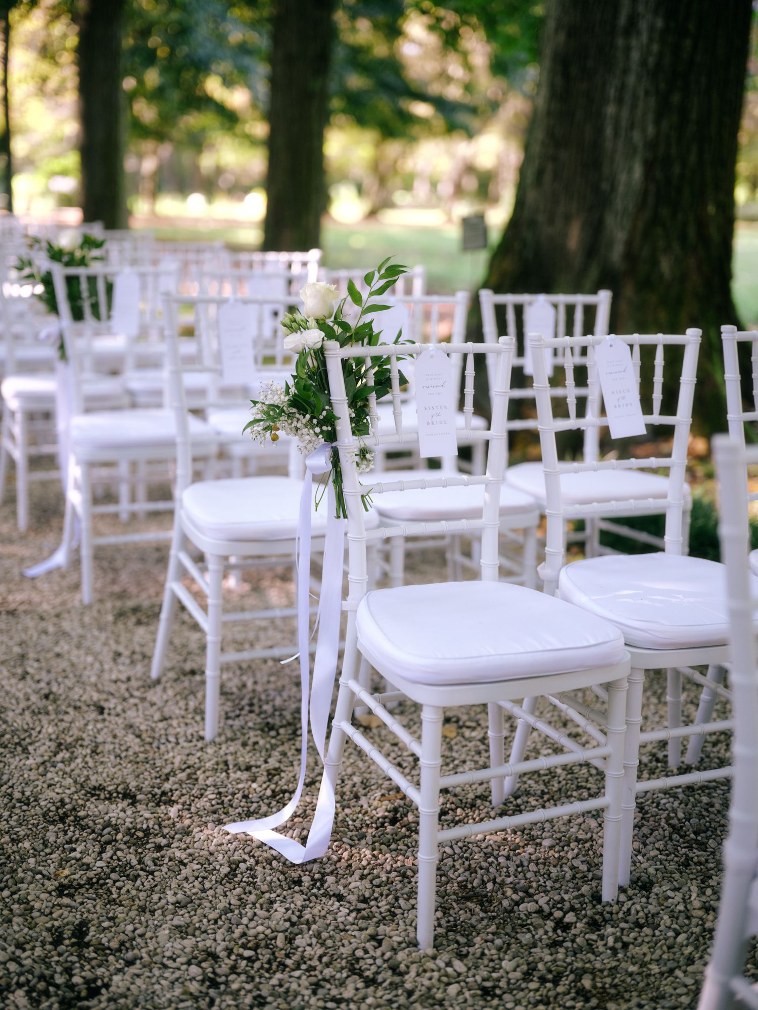 White wooden chairs arranged in rows for an outdoor wedding ceremony with delicate floral aisle decorations.