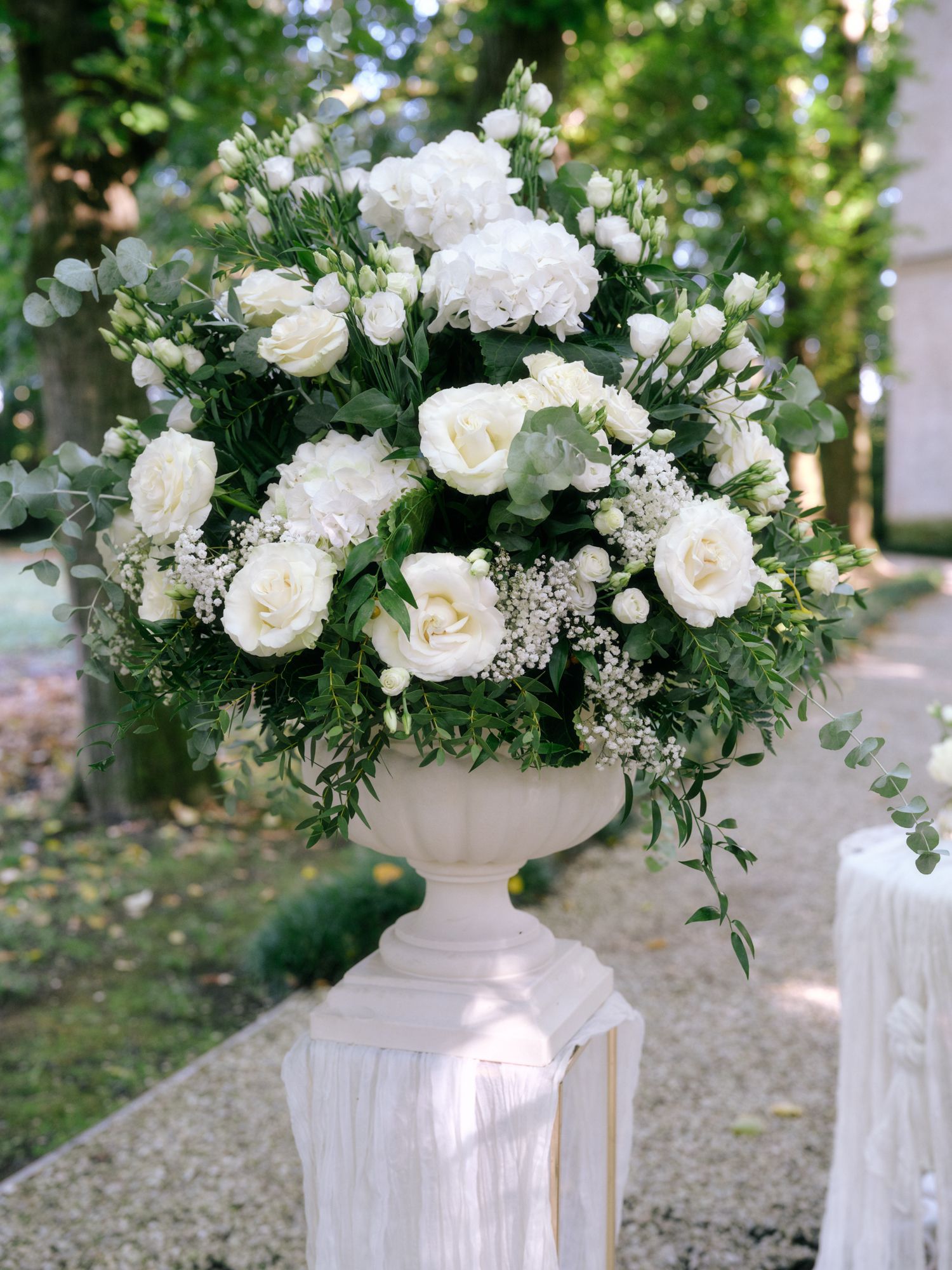 Elegant white floral arrangements in tall pedestal vases line an outdoor wedding ceremony aisle.