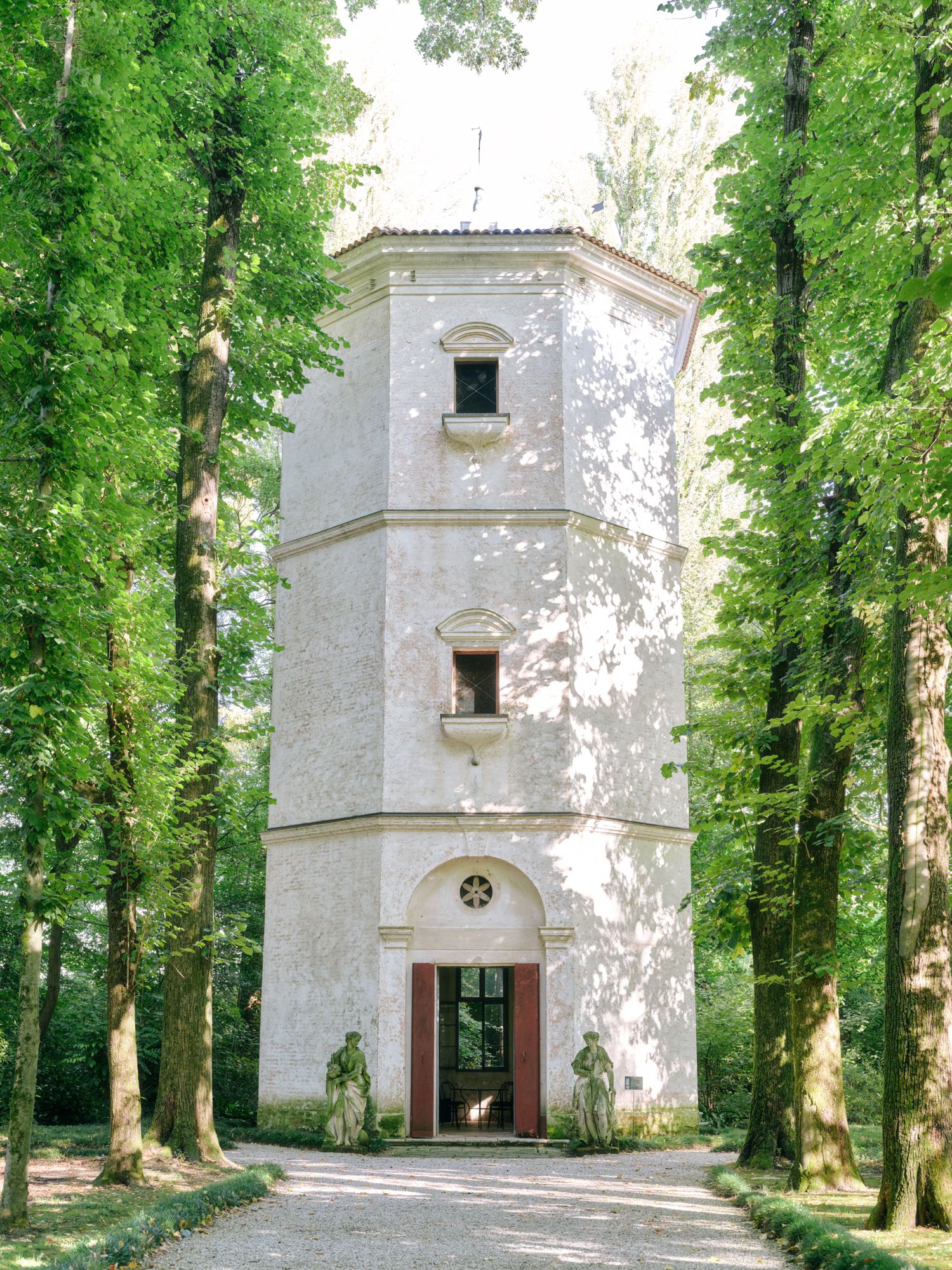A tall white octagonal tower with arched doorway stands surrounded by lush green trees in a forest setting.