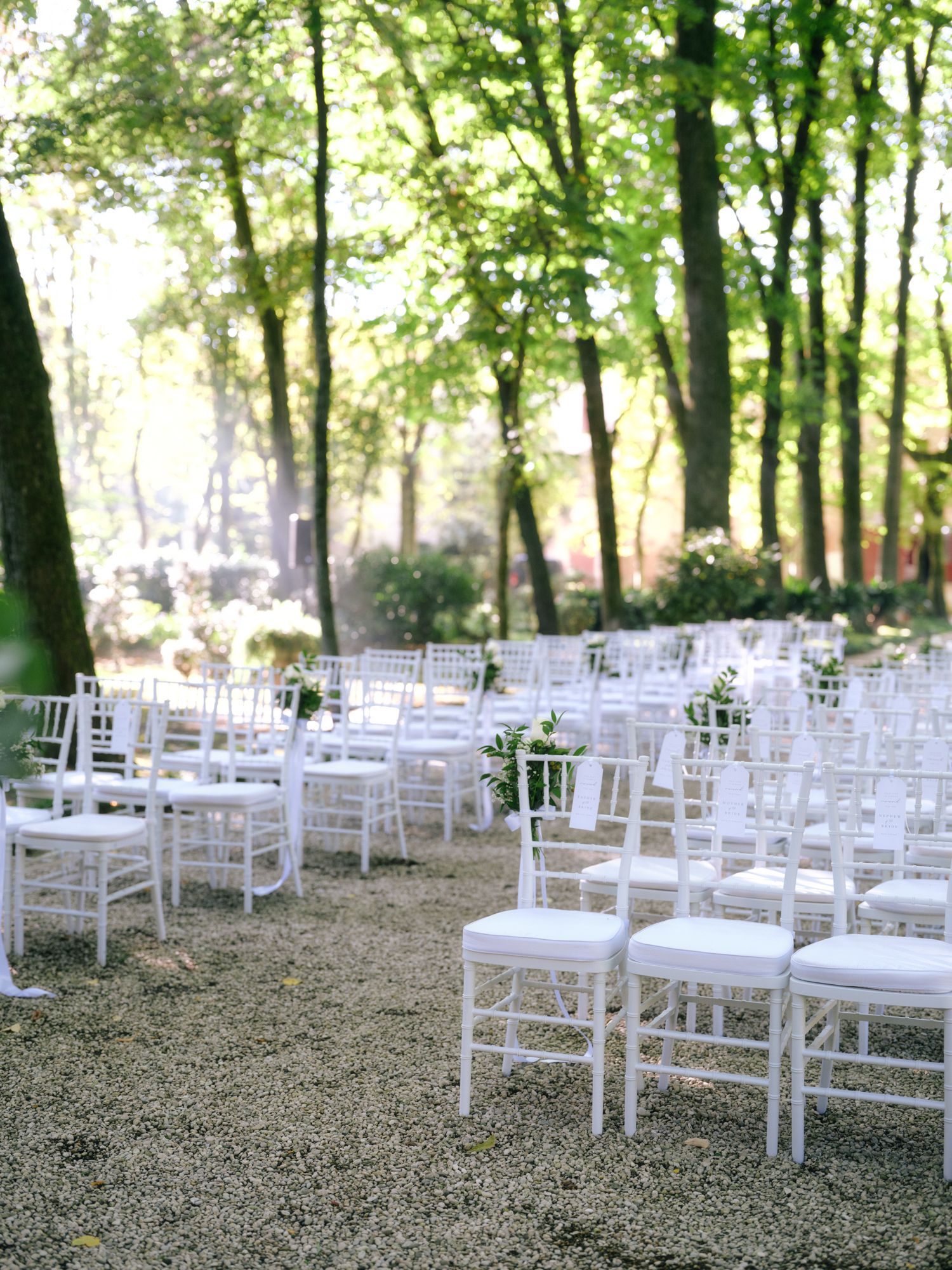 White wooden chairs arranged in rows for an outdoor wedding ceremony in a serene wooded setting.