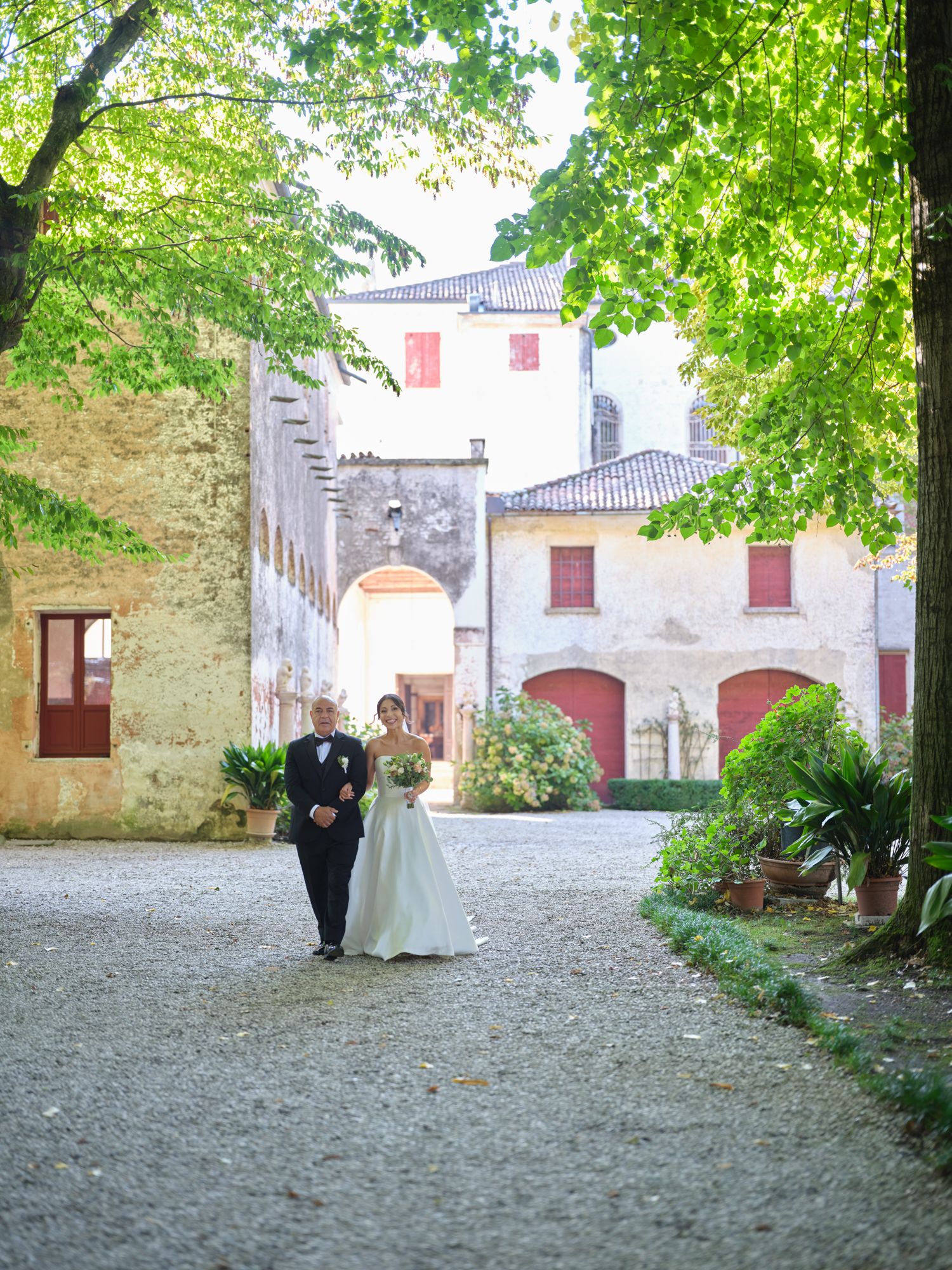 A romantic scene in an old European courtyard with stone archways and lush greenery overhead.