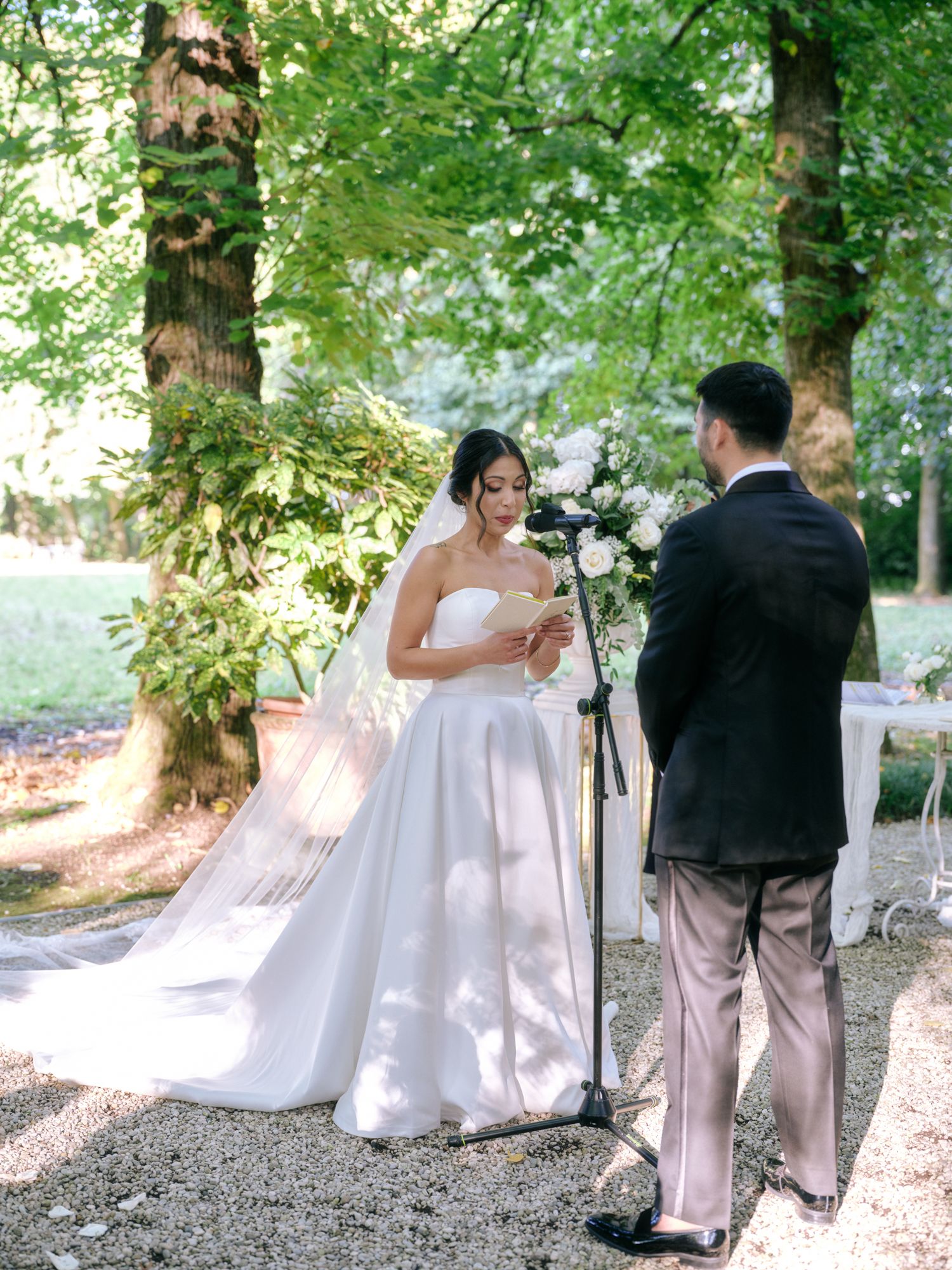 Couple in wedding attire walks hand in hand along a sunlit forest path during their outdoor photo session.