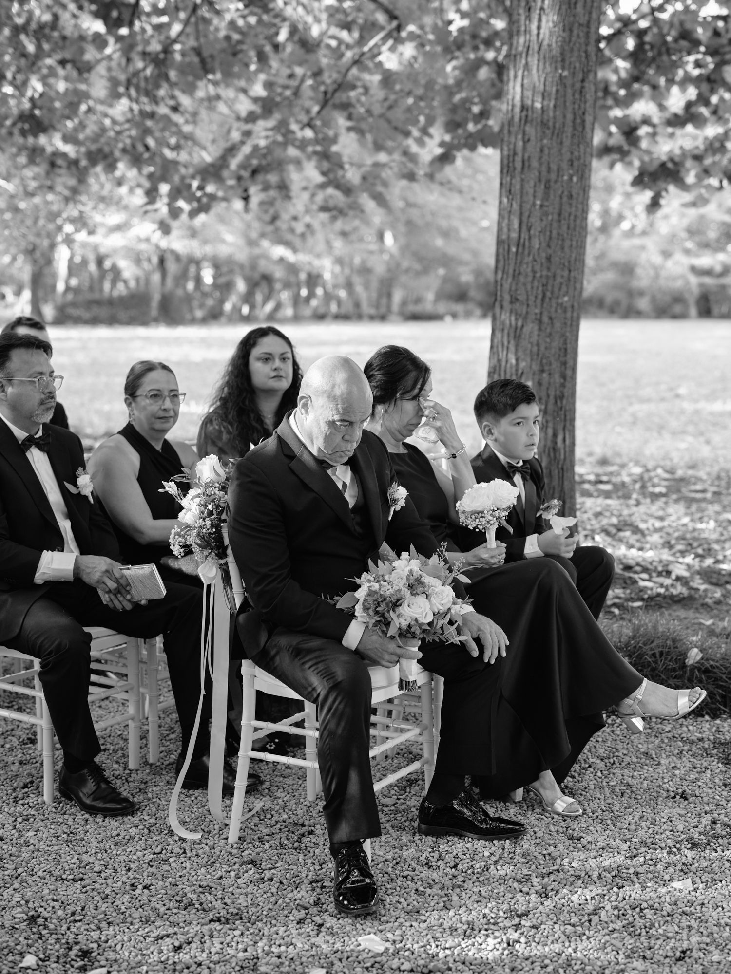 Black and white photo series of wedding party members sitting on chairs outdoors under trees during a ceremony.