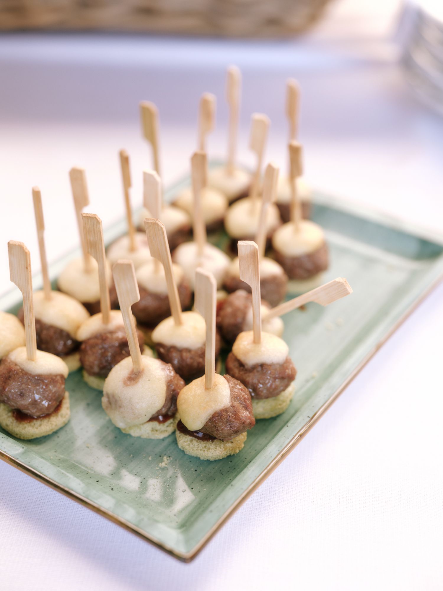 Small appetizer bites made with meatballs and mushrooms arranged on a light green serving platter with wooden toothpicks.