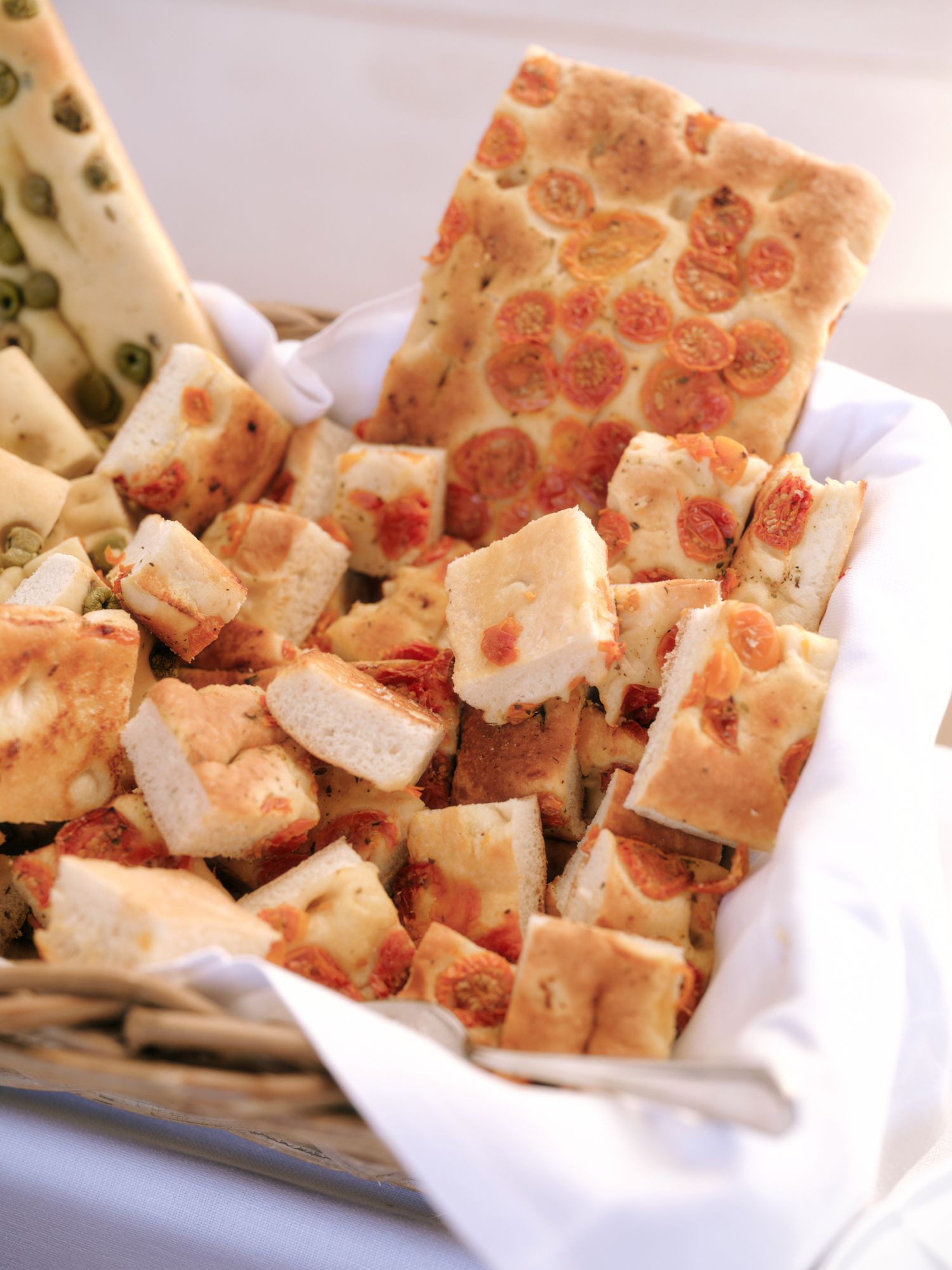 Freshly baked focaccia bread with tomatoes cut into squares and served on white parchment paper.