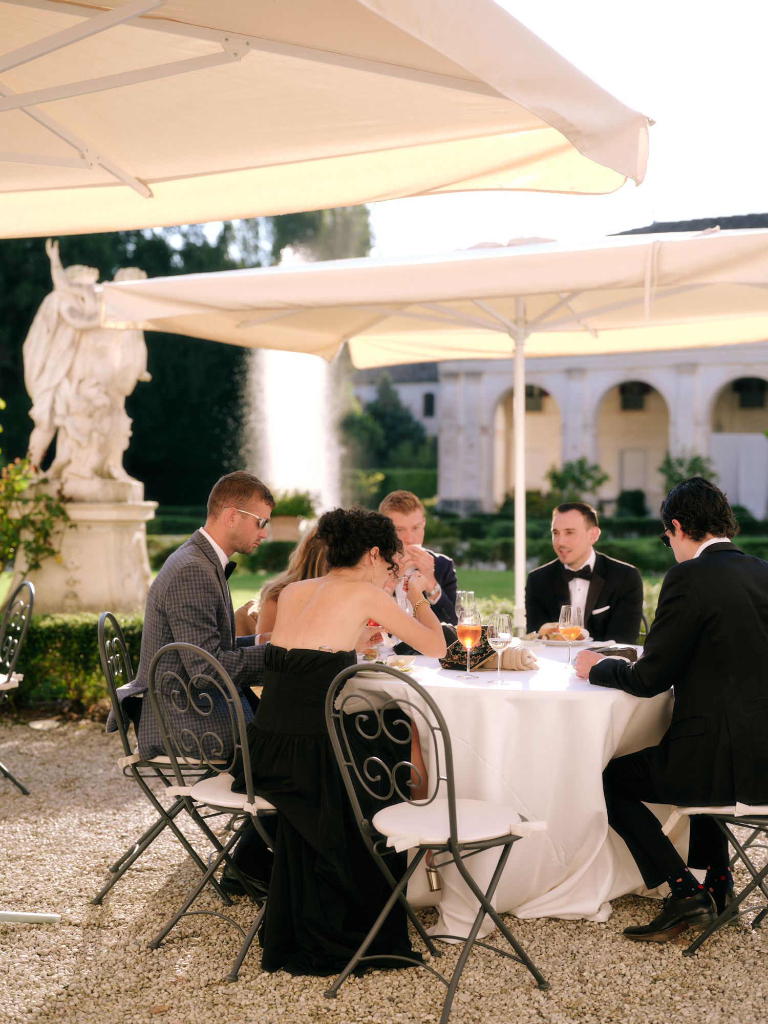 Guests seated at elegant outdoor tables during a formal event with white tablecloths and wrought iron chairs.