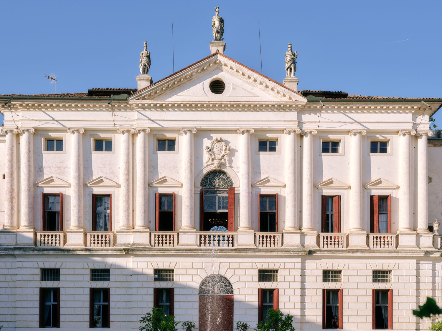 Ornate white neoclassical building facade with triangular pediment and statues on top against blue sky.