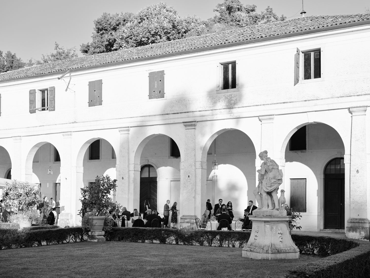 Historic white colonial building with arched porticos and columns extends along a pathway in bright sunlight.