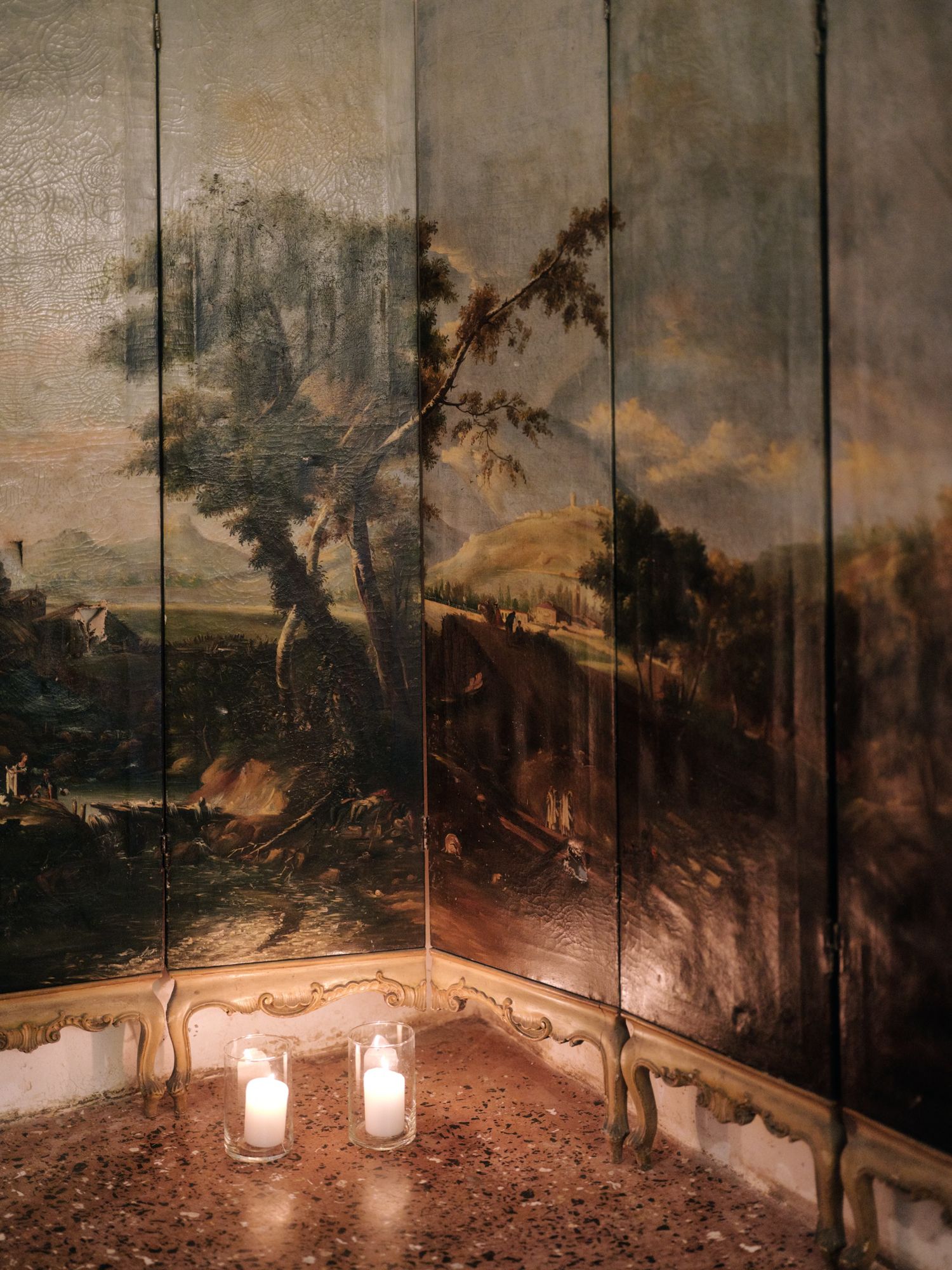 A panoramic mural depicting a moody landscape with trees and mountains adorns a curved wall illuminated by wall sconces.