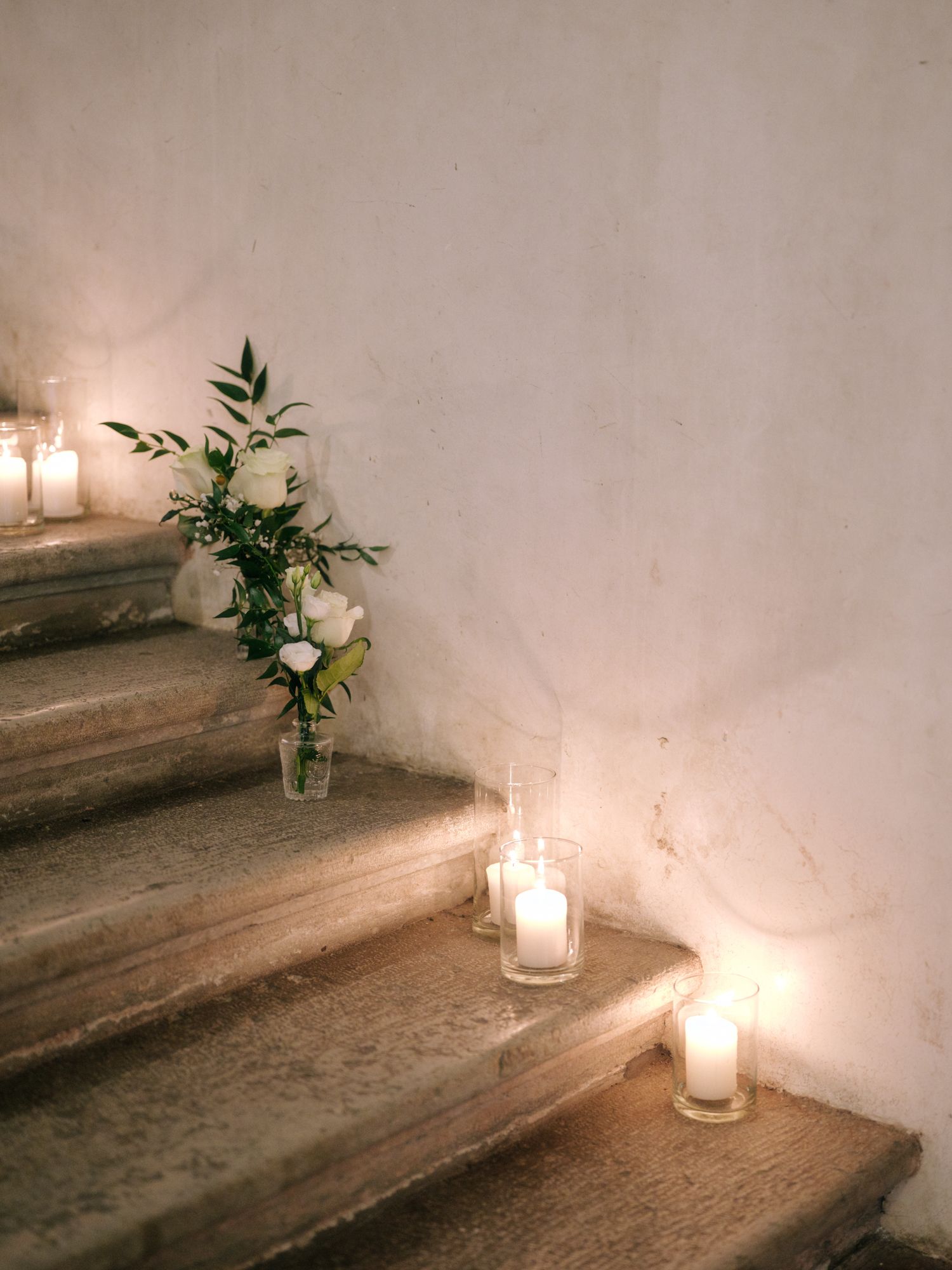 Candlelit stone steps adorned with white floral arrangements create a romantic ambiance in a dimly lit space.