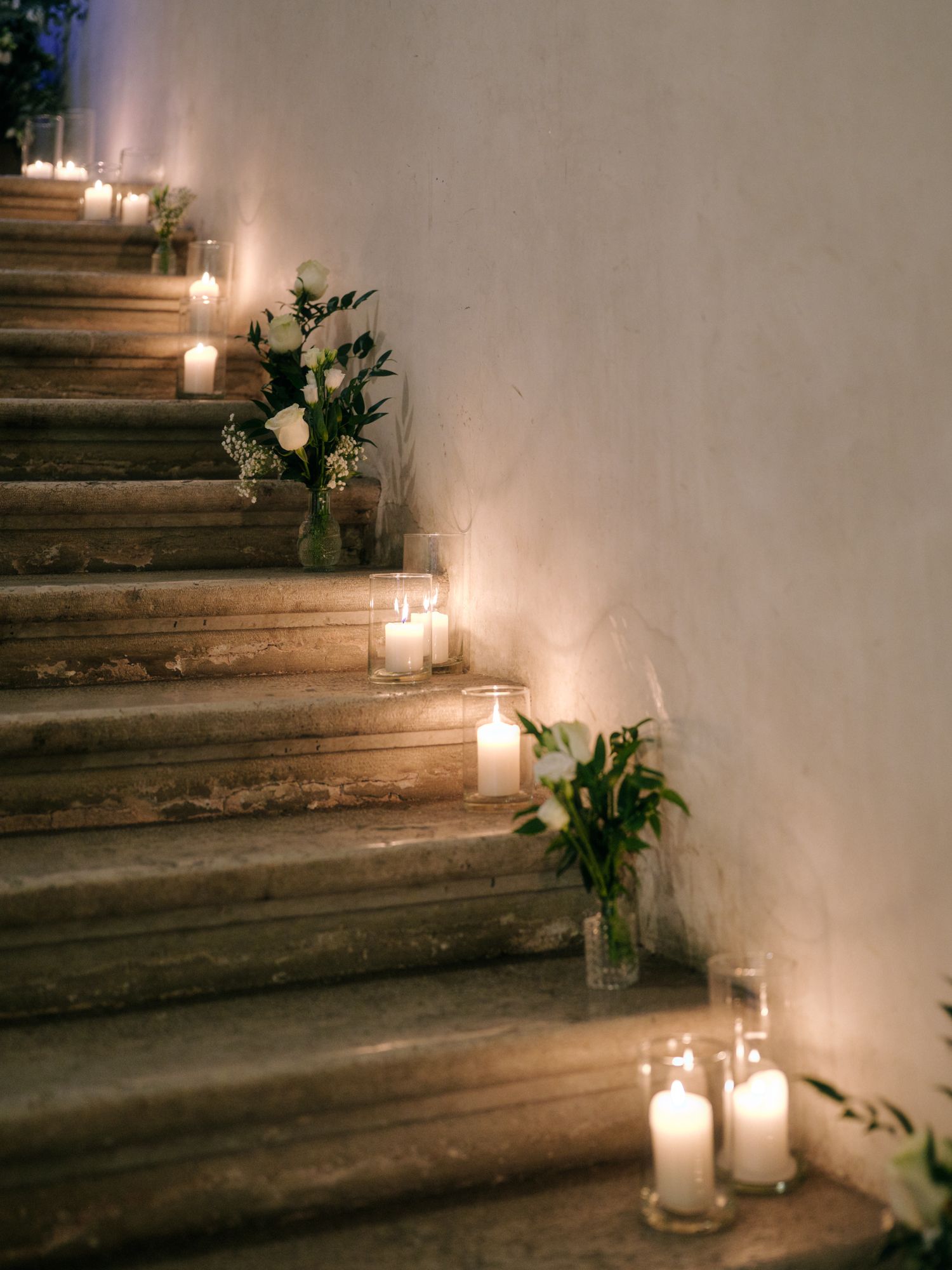 Romantic stone staircase decorated with glowing white candles and delicate floral arrangements creating an ethereal ambiance.