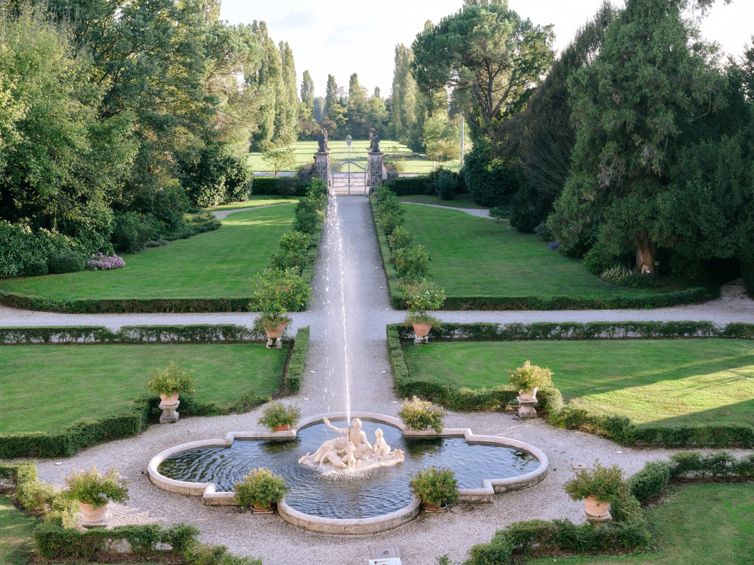 A series of connected garden pathways with circular fountains and manicured lawns surrounded by lush green trees.