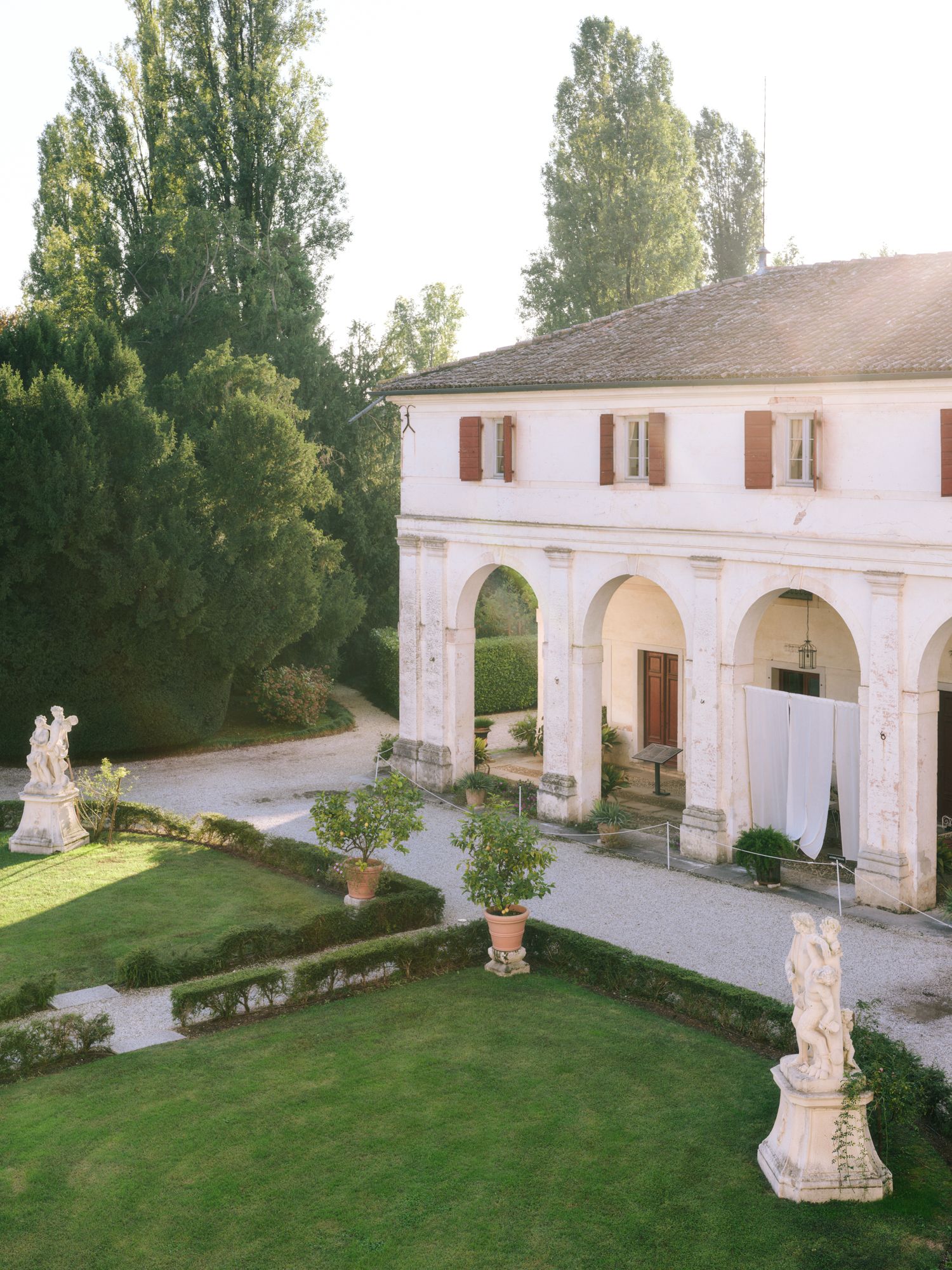 Elegant white villa with arched colonnade and classical statues adorning a manicured garden at sunset.