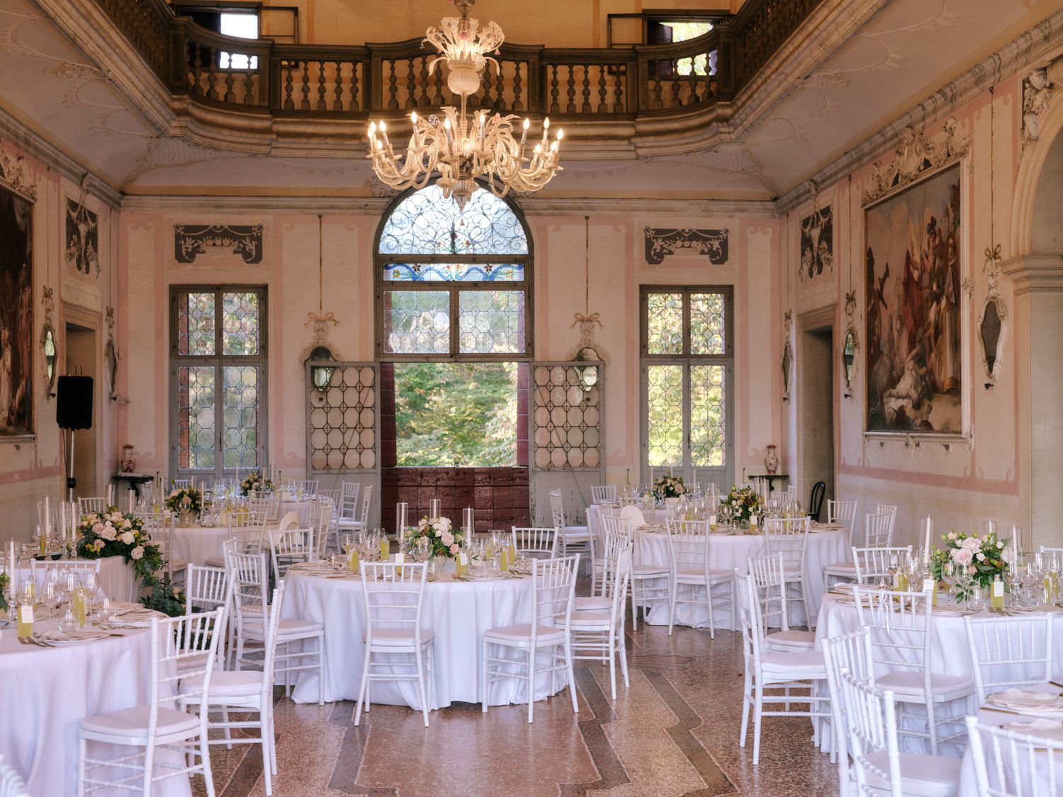 Elegant wedding reception venue with crystal chandeliers, white chairs, and panoramic windows in a luxurious ballroom setting.