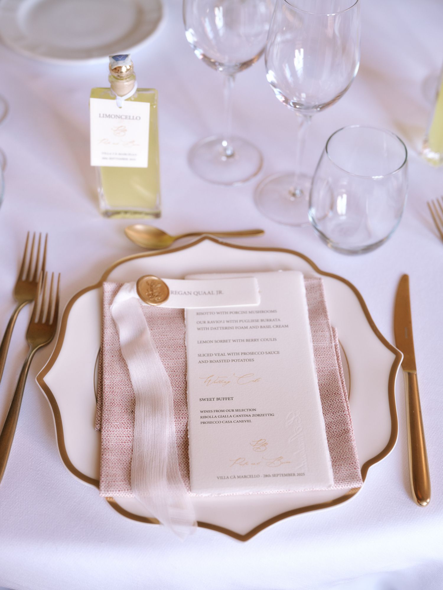 Elegant place settings with white plates, gold cutlery, and menu cards on a crisp white tablecloth at a formal event.