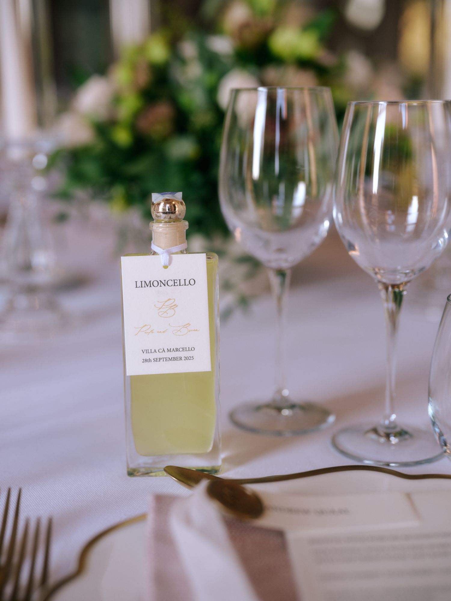 Small bottles of limoncello liqueur and wine glasses arranged on an elegant white tablecloth at a formal dining setting.