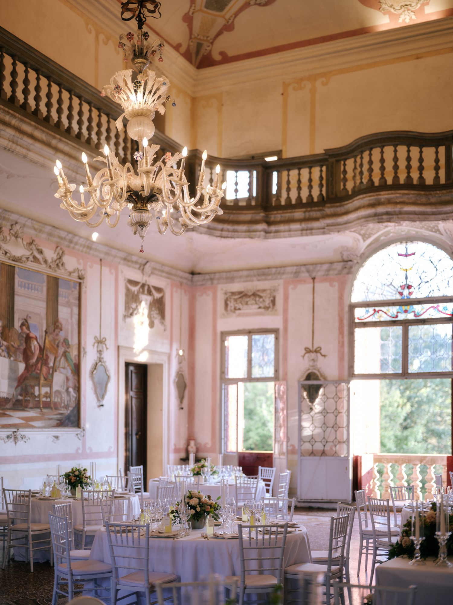 Elegant white ballroom with crystal chandeliers and round dining tables set for a formal wedding reception.