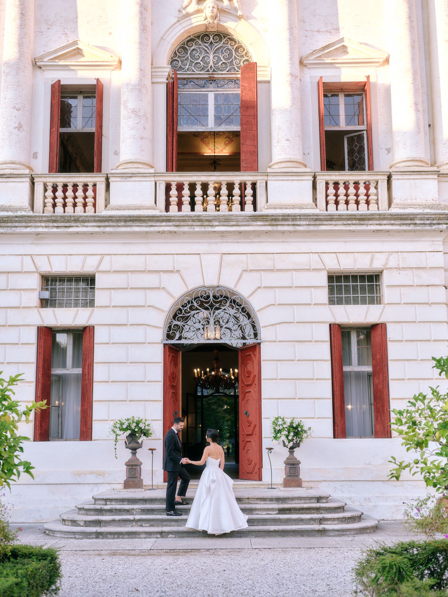 Elegant couple in formal attire walk up grand stone steps of historic building with ornate architectural details.