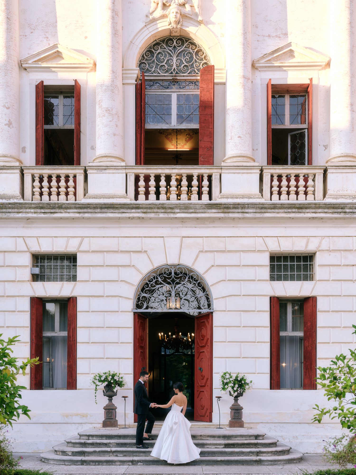 A white wedding dress is photographed in front of an elegant historic building with classical columns and stone balustrades.
