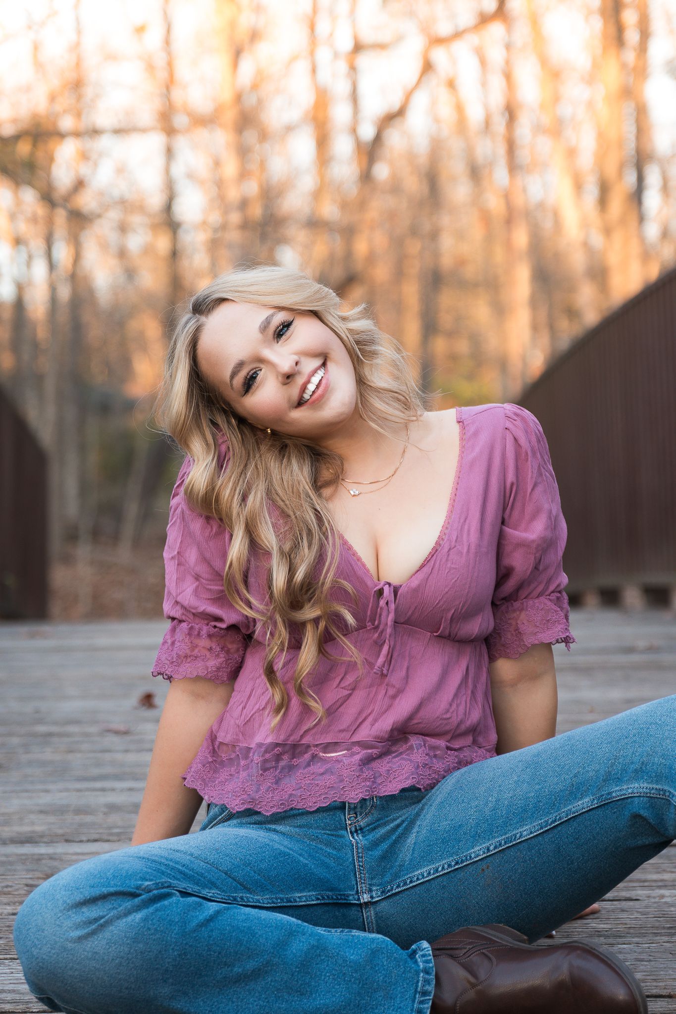 Senior girl sits on a bridge for senior photos at Parker Mill County Park in Ann Arbor. She is smiling and wearing a pink shirt in the fall.