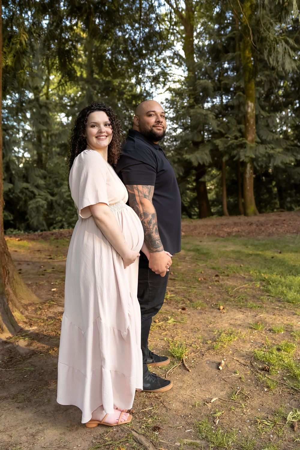 A couple shares an intimate moment in a wooded outdoor setting wearing black and light pink outfits.