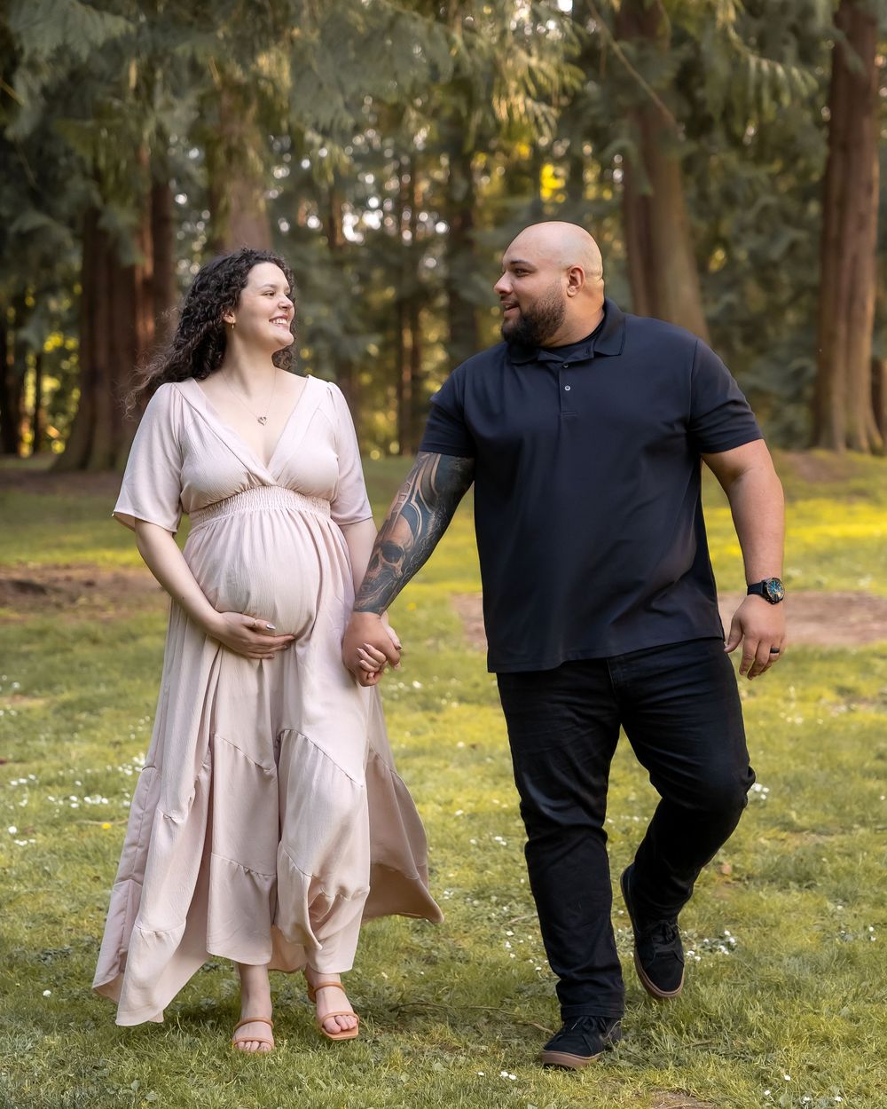 A couple in beige and black outfits shares playful moments together while walking through a sunlit park.