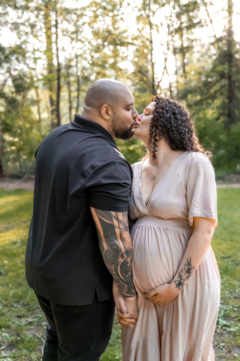 A tender maternity photoshoot in nature with a couple embracing in soft evening light.