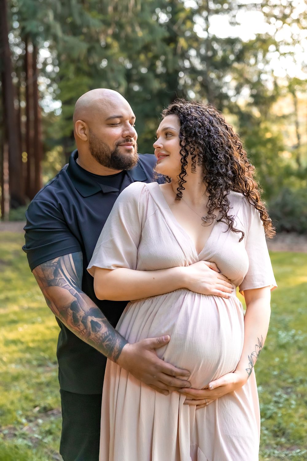 Romantic outdoor maternity photos showing loving couple embracing in a sunlit forest setting.