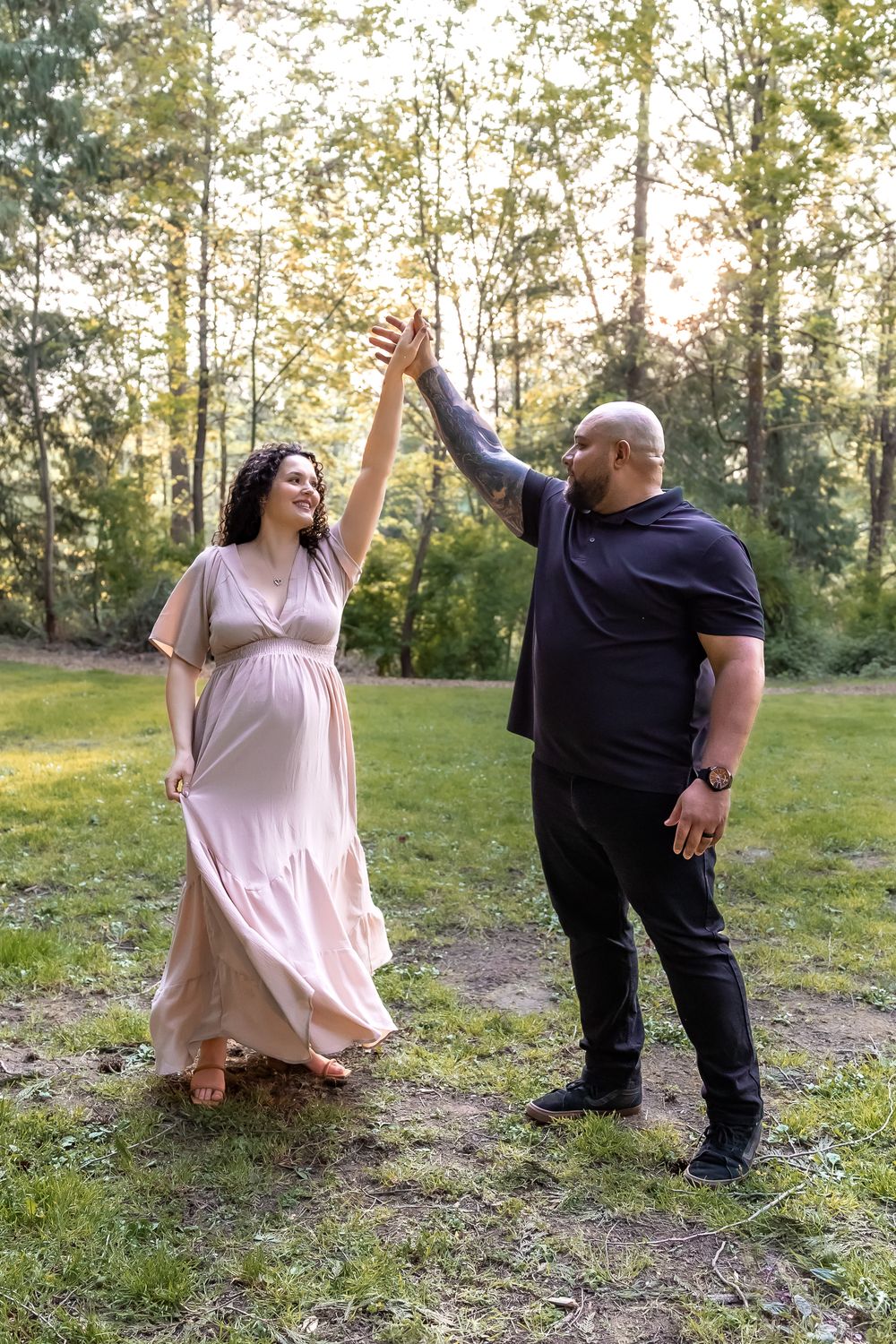 A couple dances joyfully together in a sunlit forest clearing during golden hour.