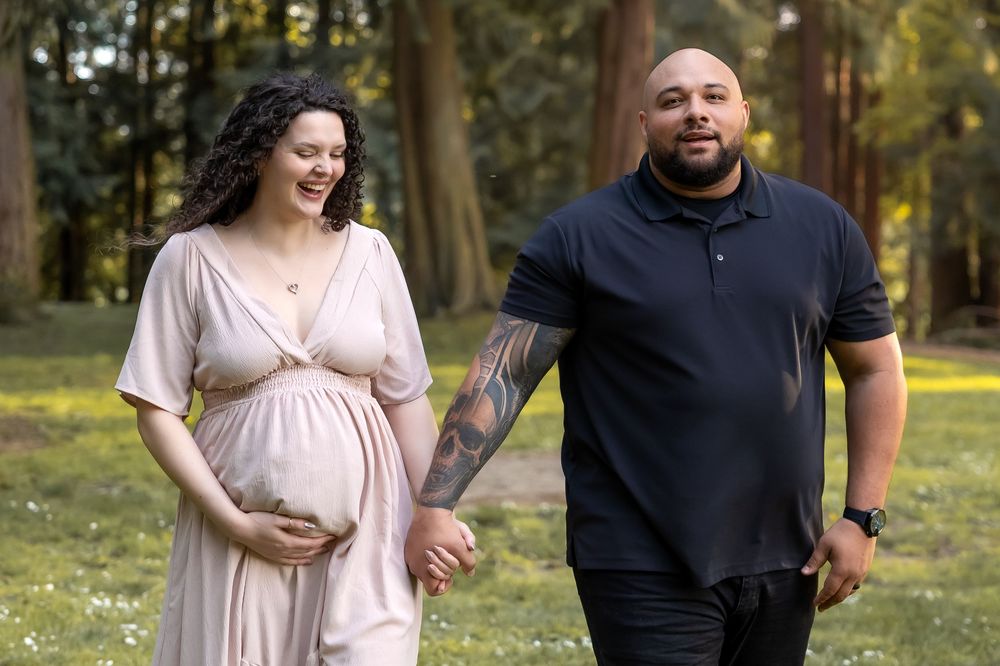 A couple in casual attire smiling and walking together in a sunny park with trees in the background.