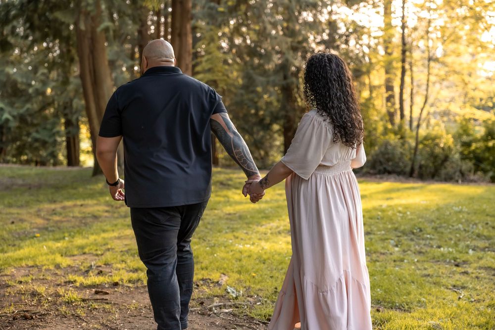 A couple walks hand in hand through a sunlit meadow during golden hour.
